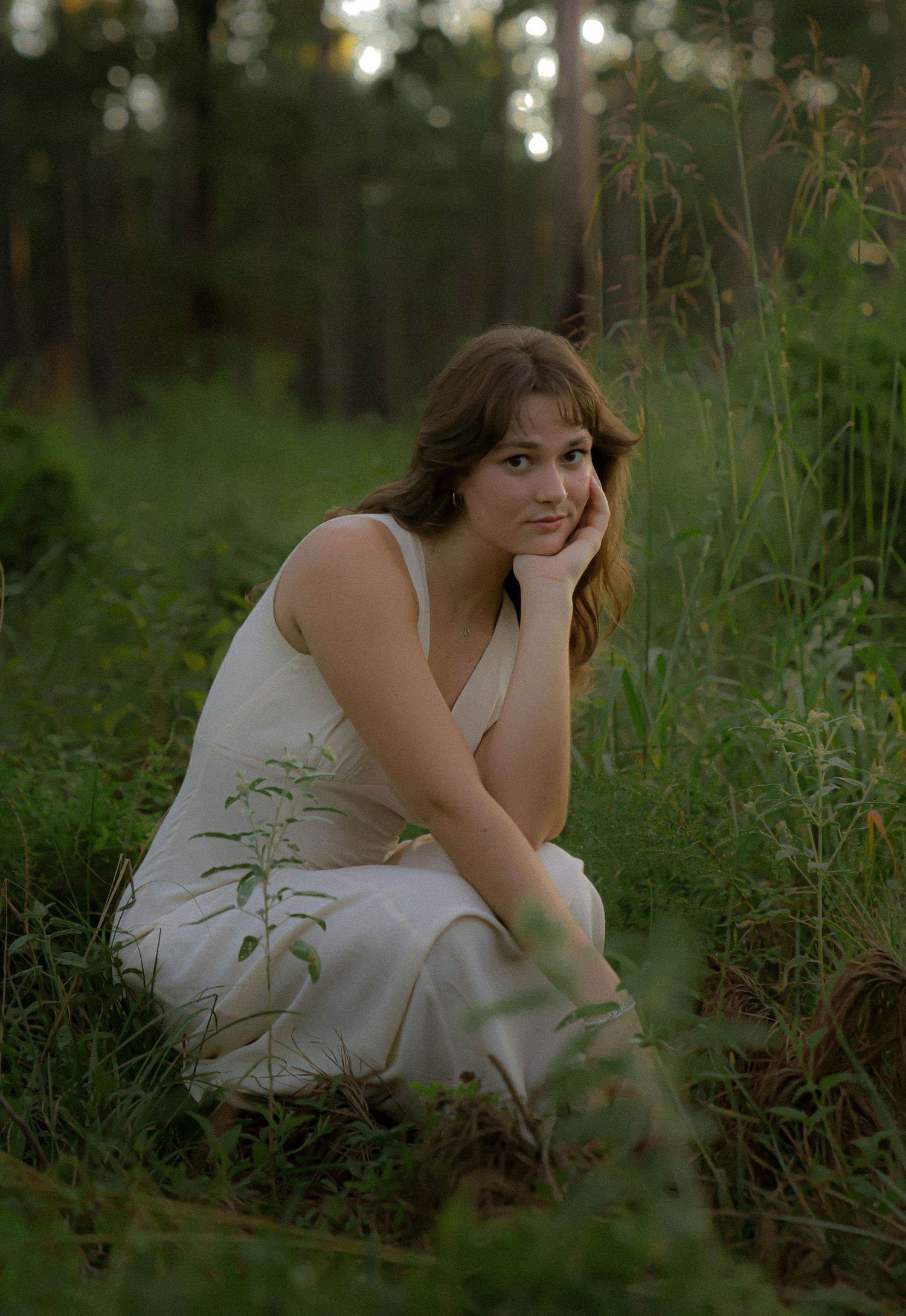 Serene outdoor portrait in a white dress surrounded by forest greenery at dusk.