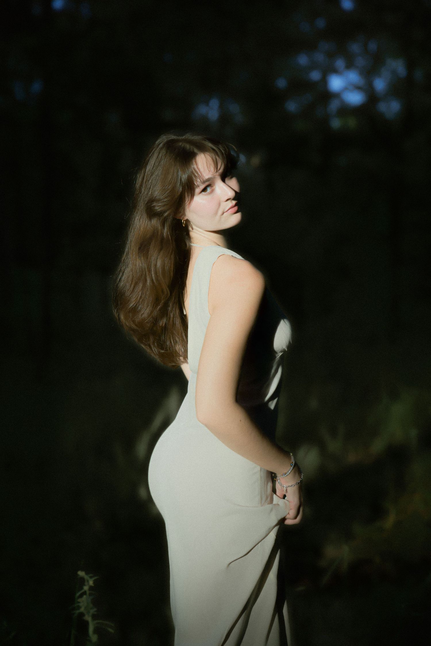 Artistic portrait of a white dress against a dark moody background in a natural outdoor setting.