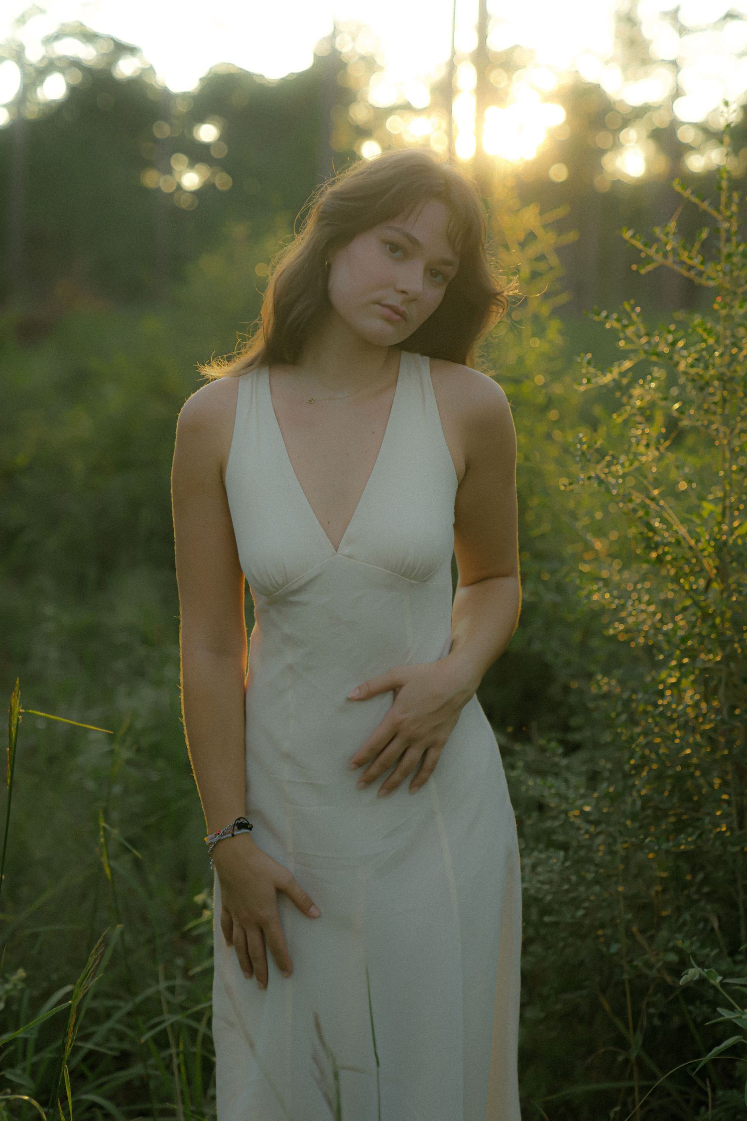 Soft golden hour portrait in a white dress amid wild summer foliage.