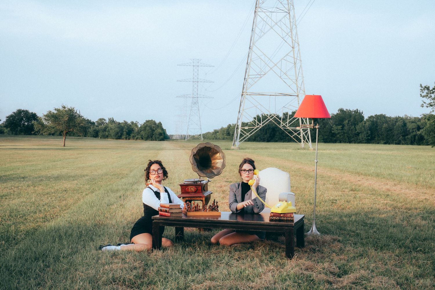 People enjoying a picnic on a wooden bench under a high voltage power transmission tower in an open field.