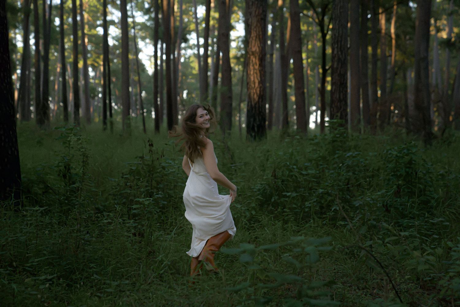 Dreamy forest scene with white dress flowing through green undergrowth.