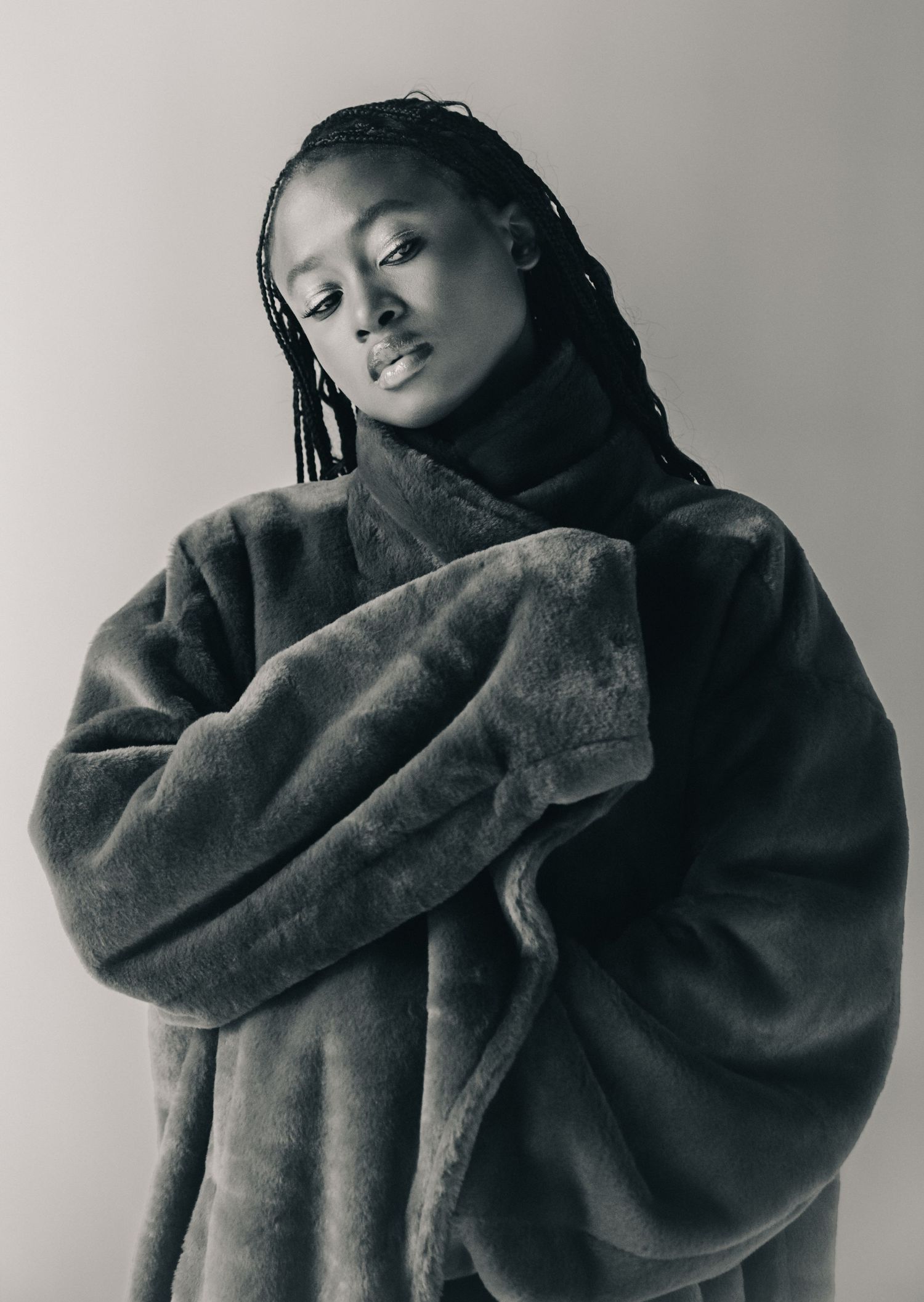 A person wearing a cozy gray faux fur coat poses in a series of artistic black and white portraits.