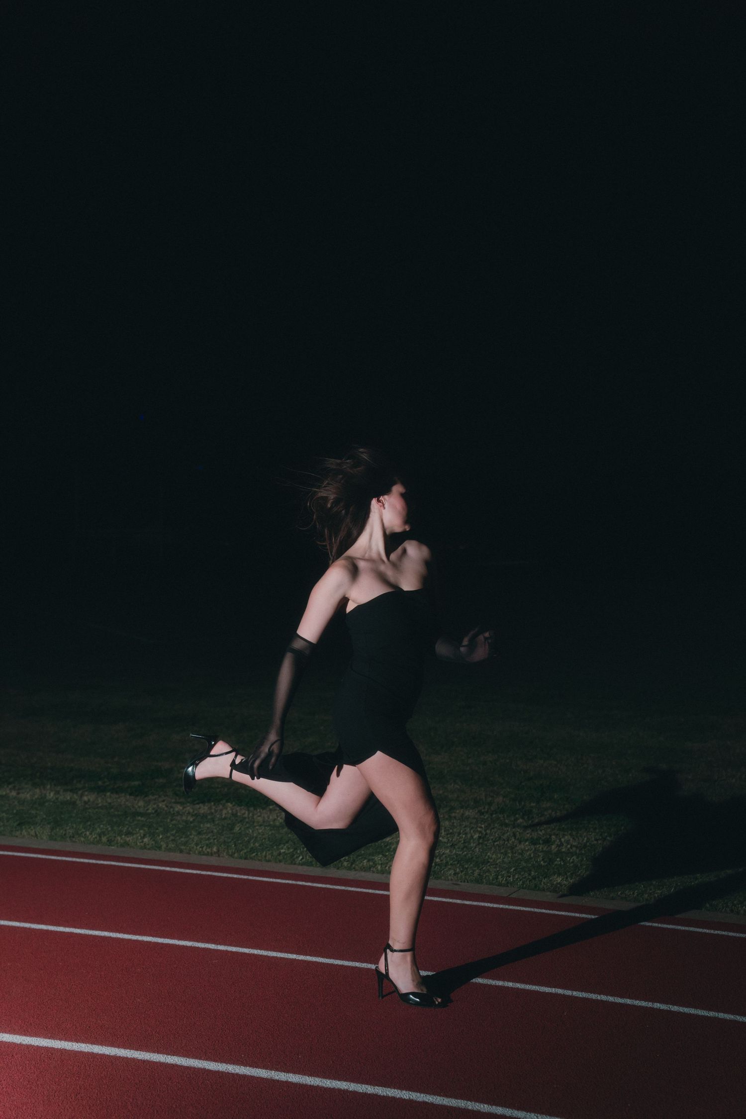 Sequence of an athlete performing a backflip on a dark track at night with dramatic shadows and lighting.