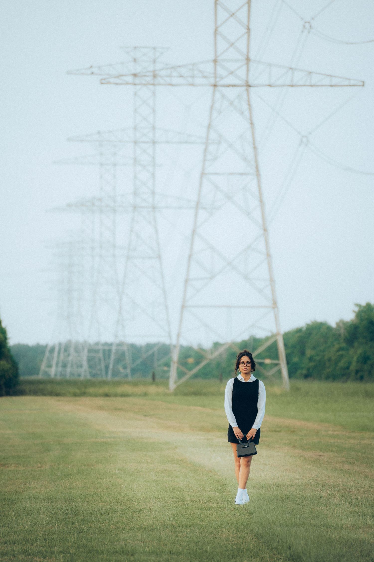 Tall electrical transmission towers rise against a cloudy sky over green grass field.