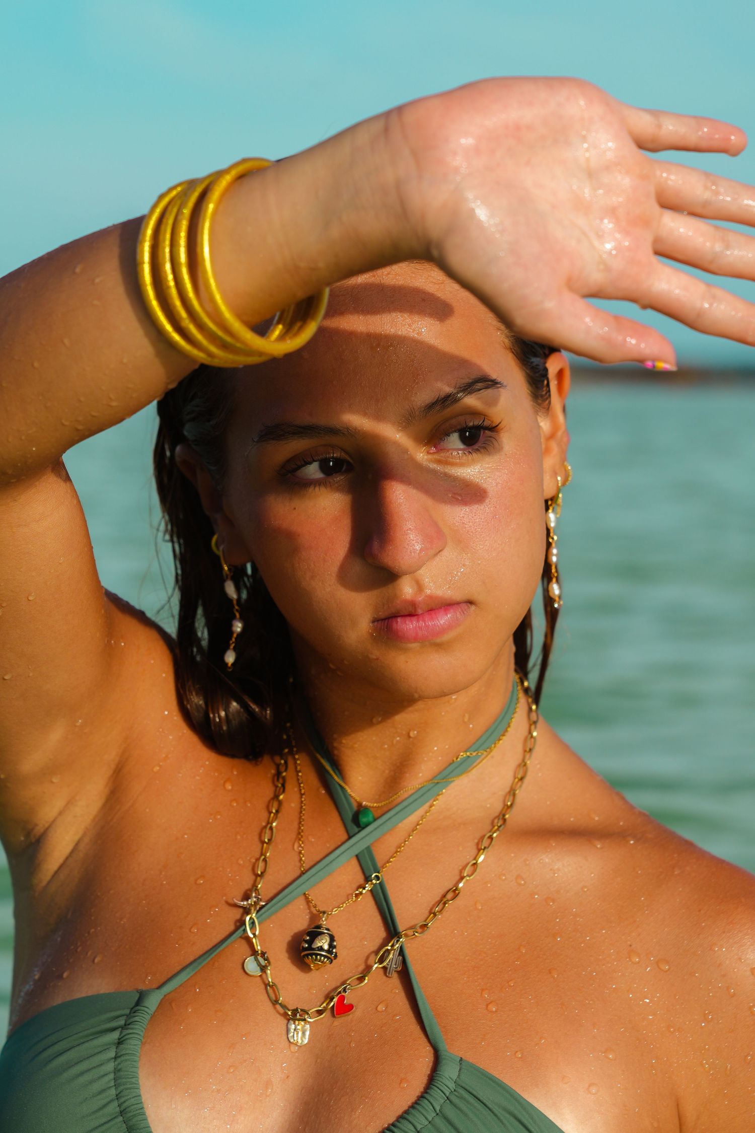Summer beach portrait with gold bangles and jewelry against turquoise water.