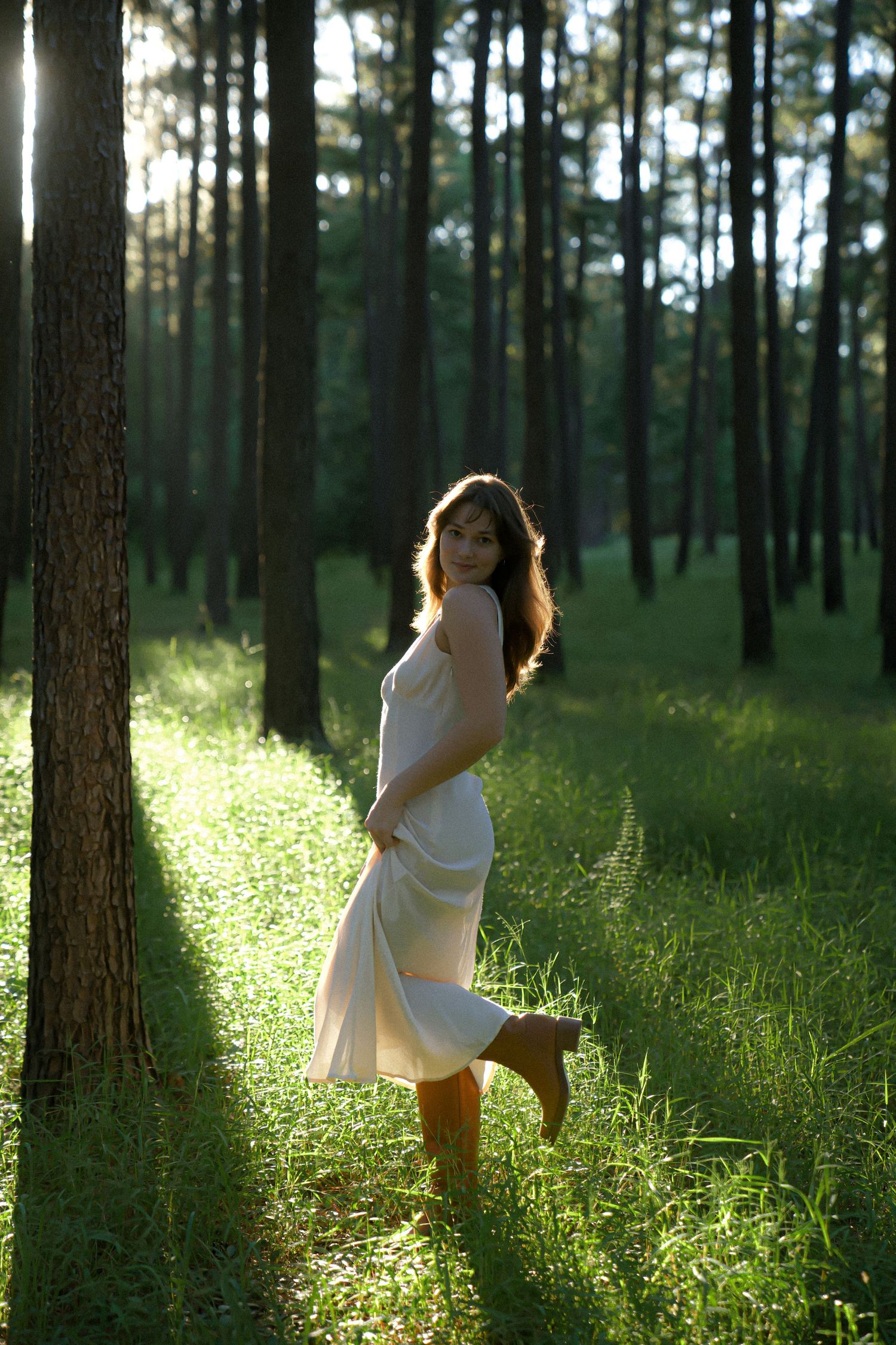 A dreamy forest scene shows a flowing white dress catching golden light between pine trees.