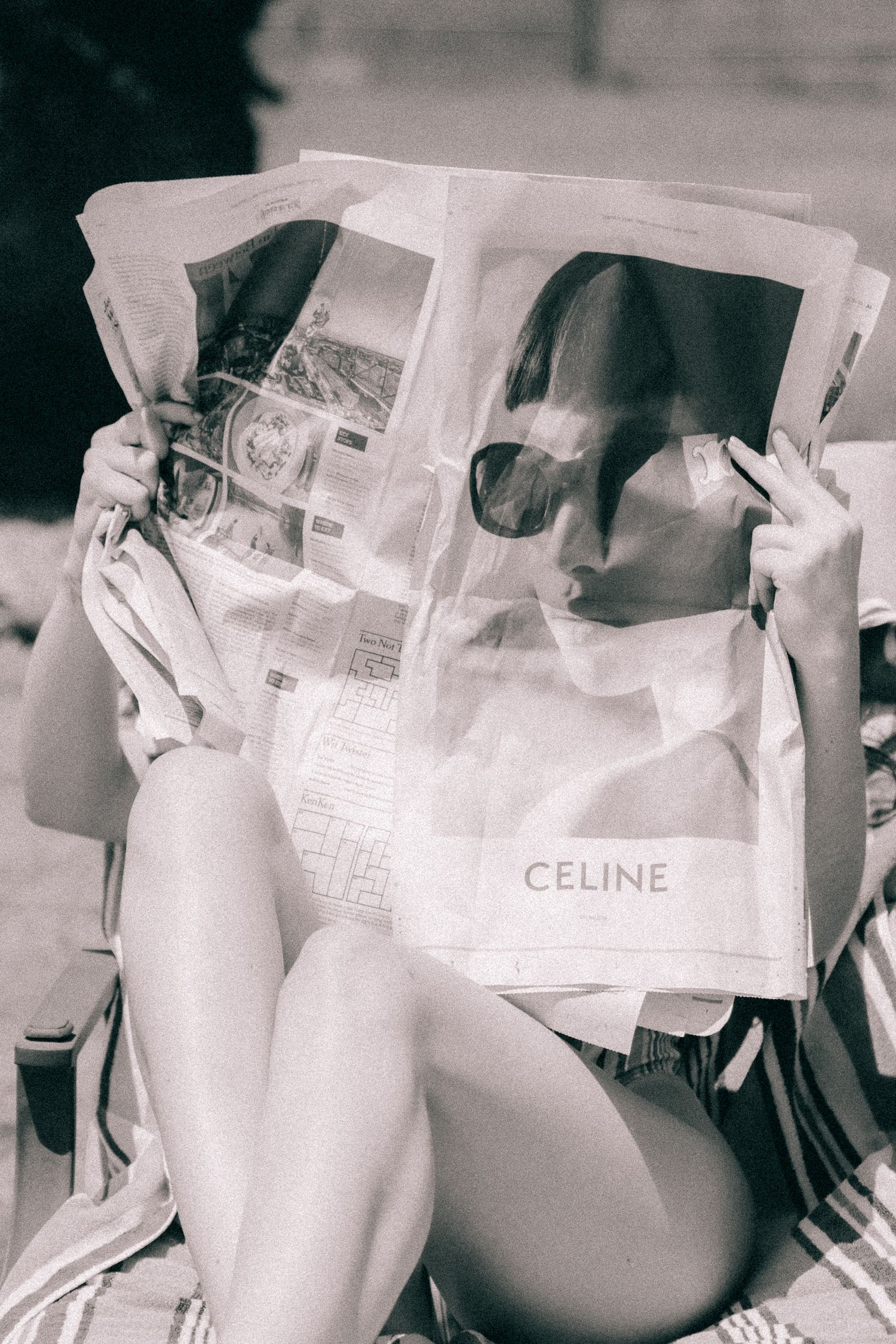 Woman reading fashion magazine with Celine branding while relaxing in black and white vintage style photo.