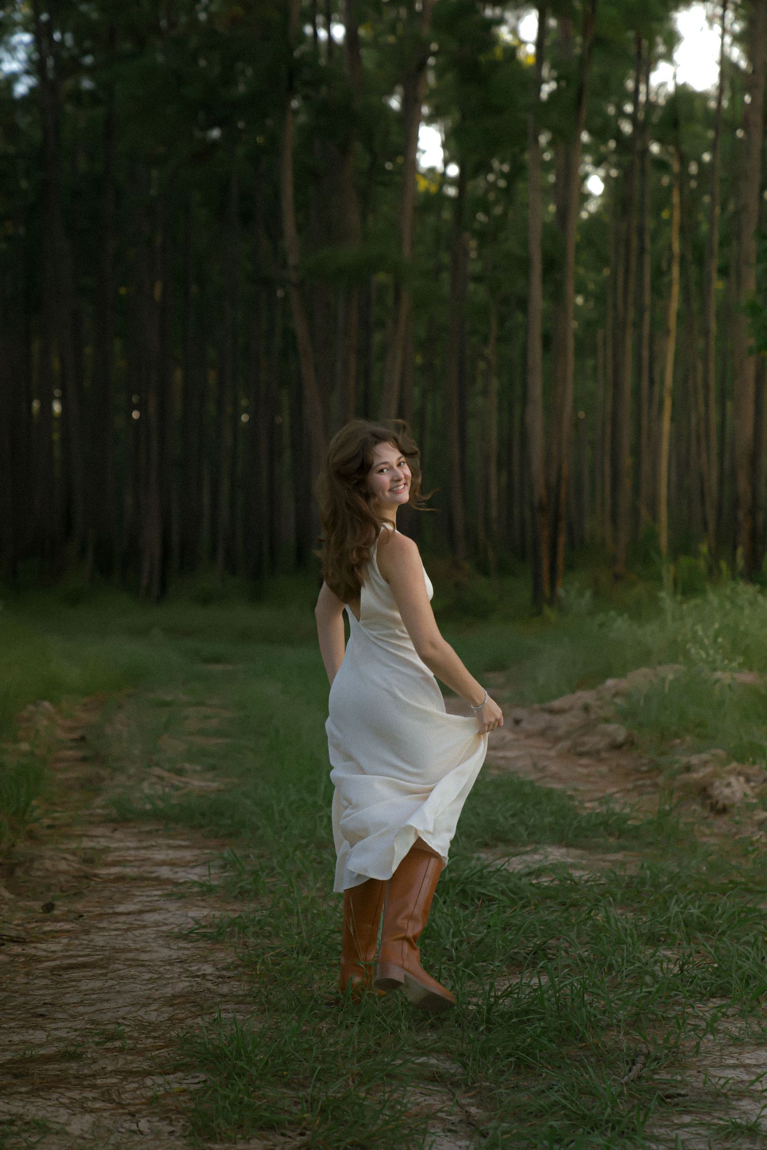 Whimsical movement on a forest path with white dress flowing in evening light.