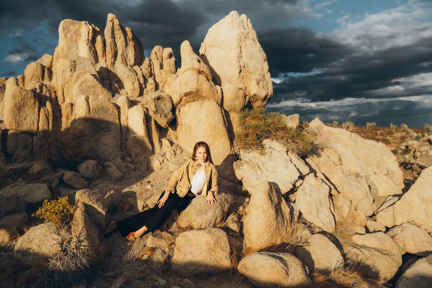 Dramatic rock formations in Joshua Tree National Park glow golden in warm sunlight against a moody cloudy sky.