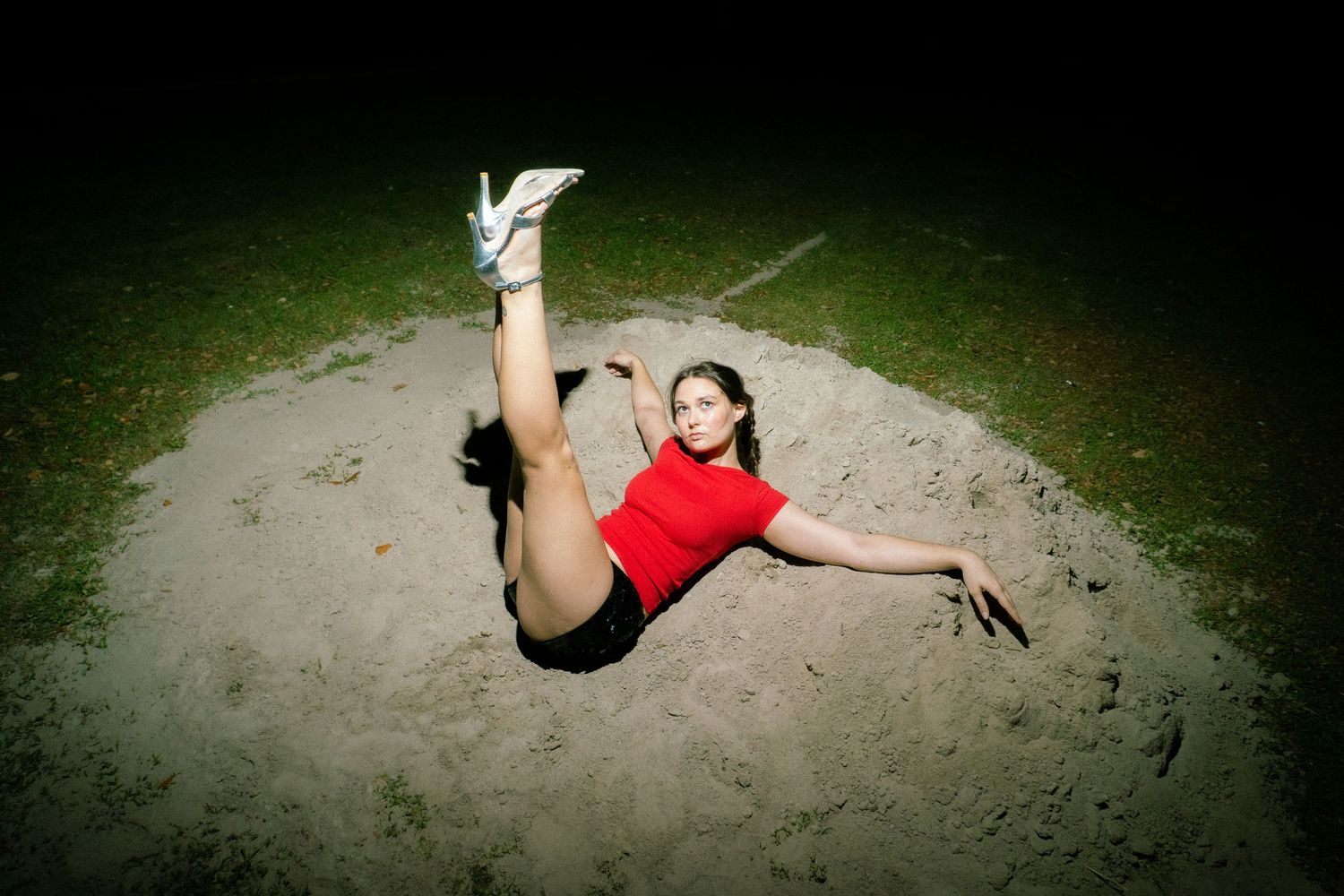 A dancer in a red top performs a dynamic leap against a dark background with dramatic lighting.