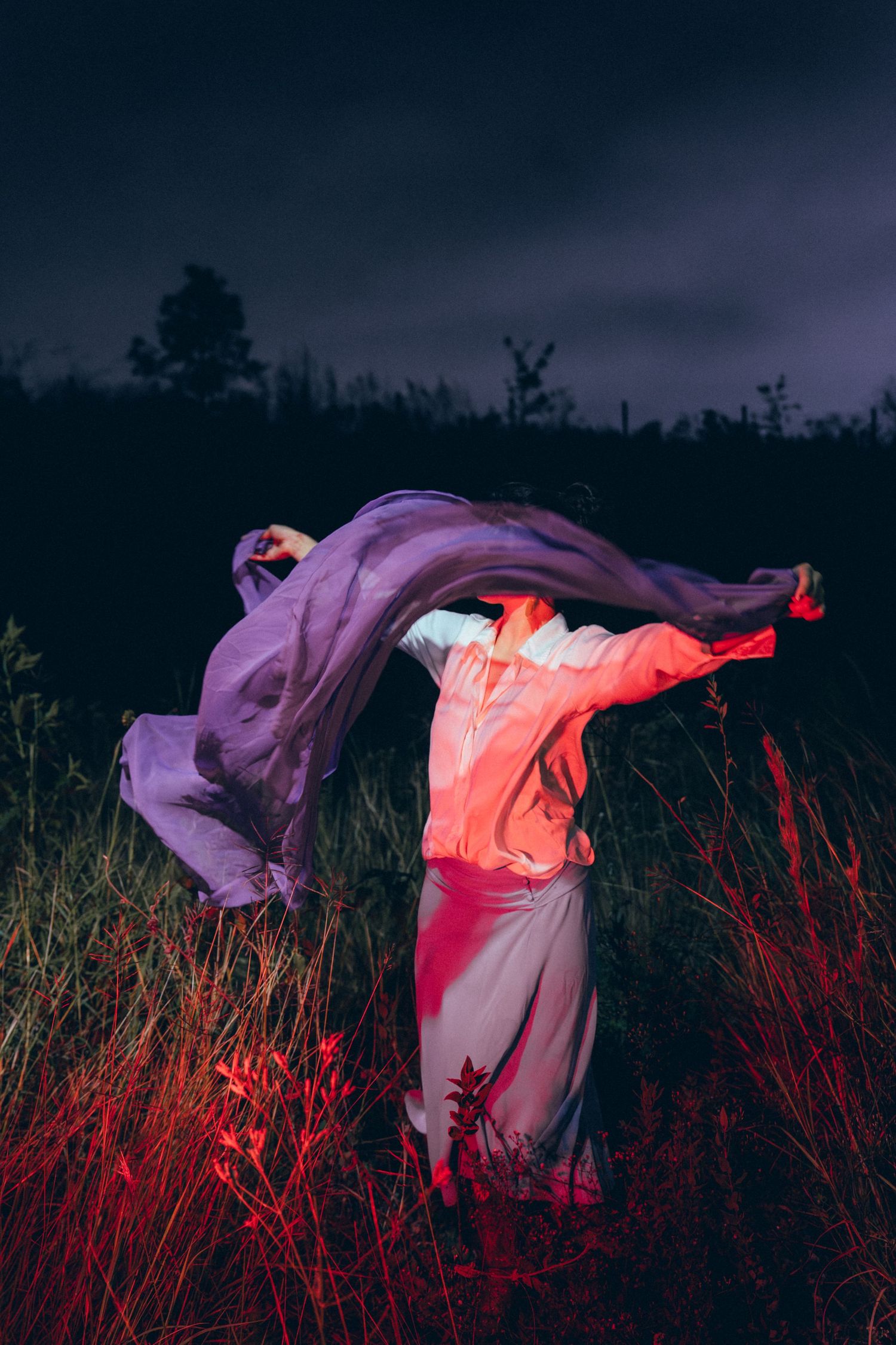 Ethereal figure in flowing white and pink fabric dances dramatically against dark moody landscape at dusk.