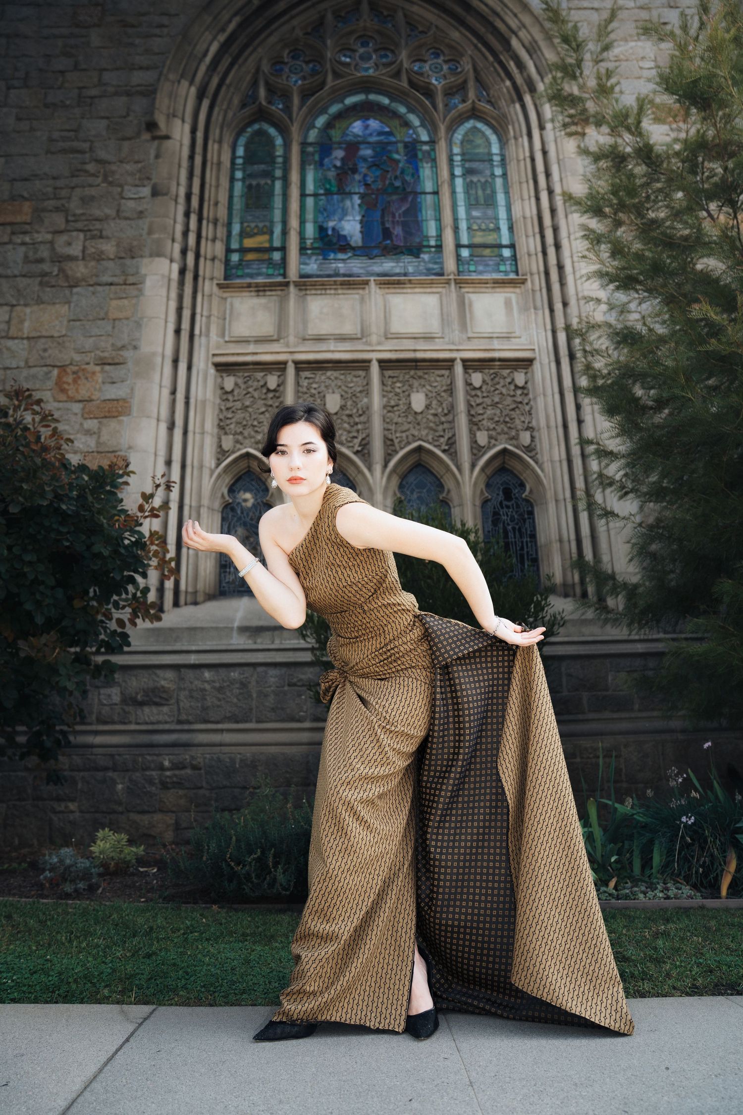 A figure in a polka dot dress poses dramatically against a gothic church exterior with stained glass windows.