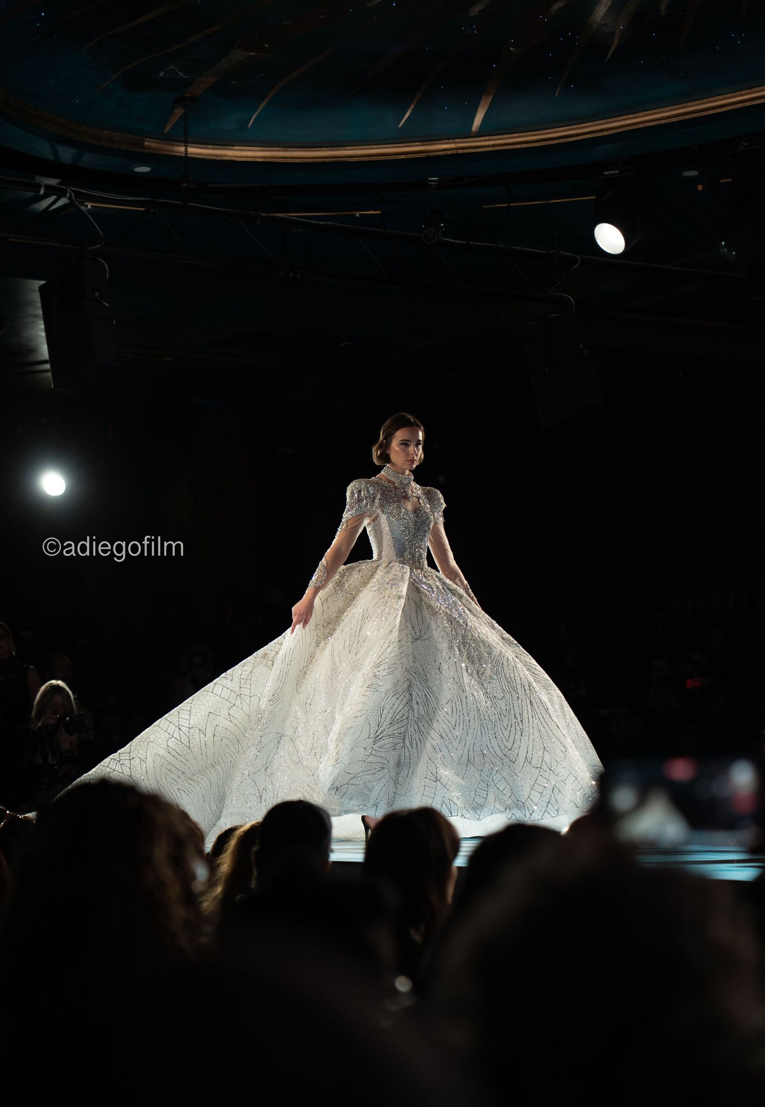 A model walks the runway in a dramatic white gown with wing-like fabric panels that billow out during the fashion show.