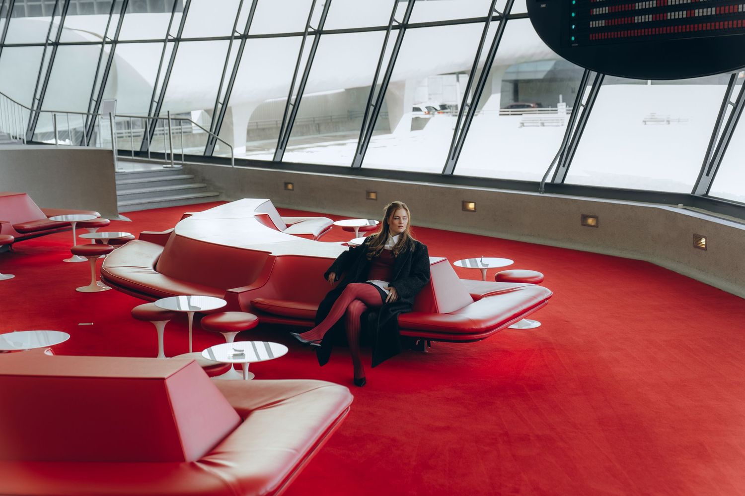 Modern office space with curved red carpet and white furniture features panoramic windows and contemporary design elements.