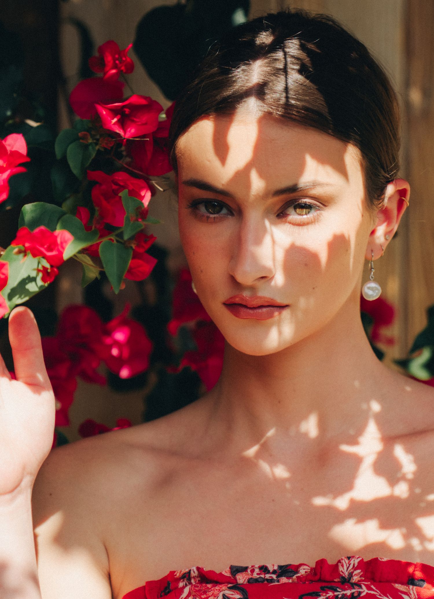 Portrait of a woman in natural lighting with red roses and dappled shadows falling across her face and shoulders.
