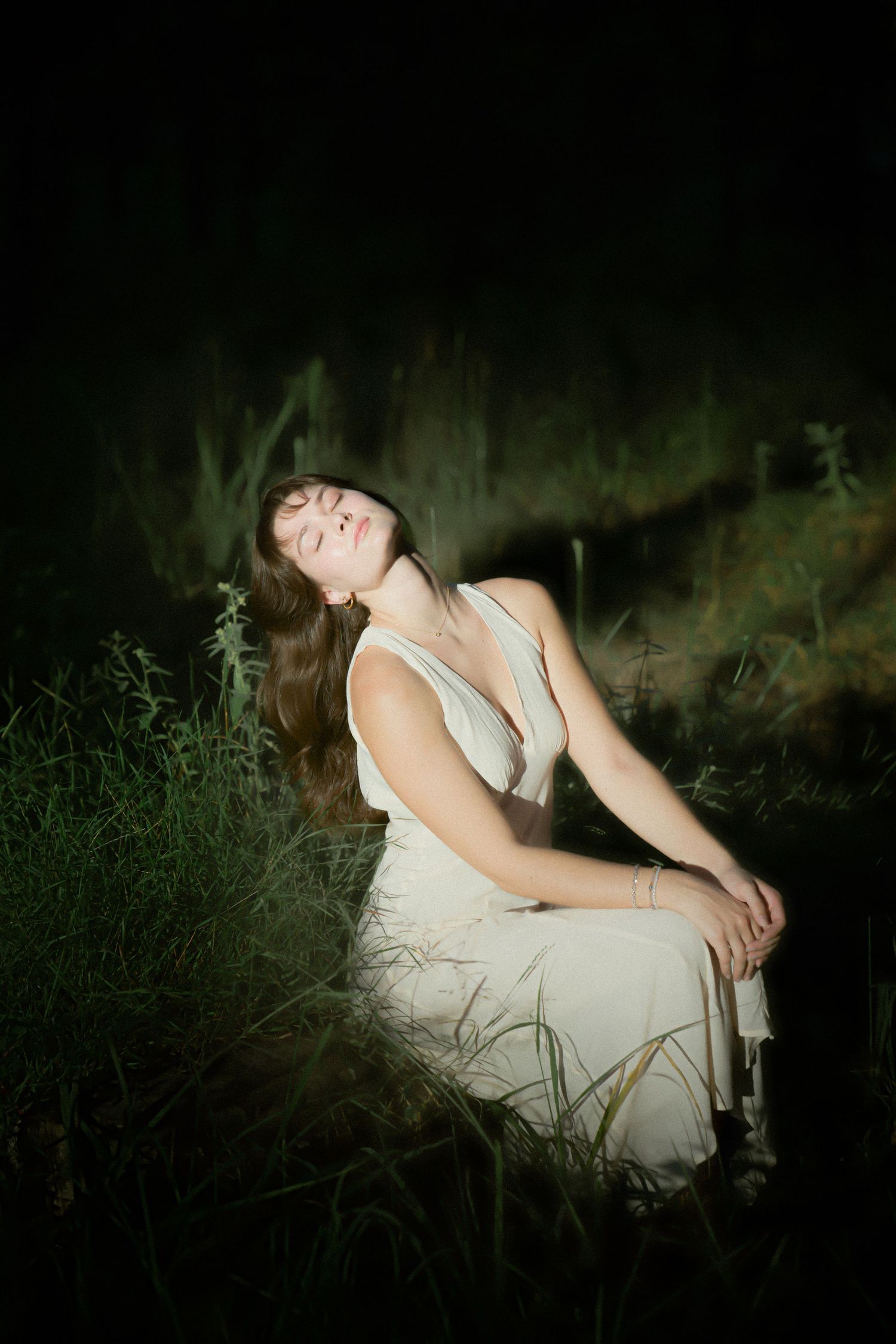 Dramatic evening portrait with white dress against dark moody natural backdrop.