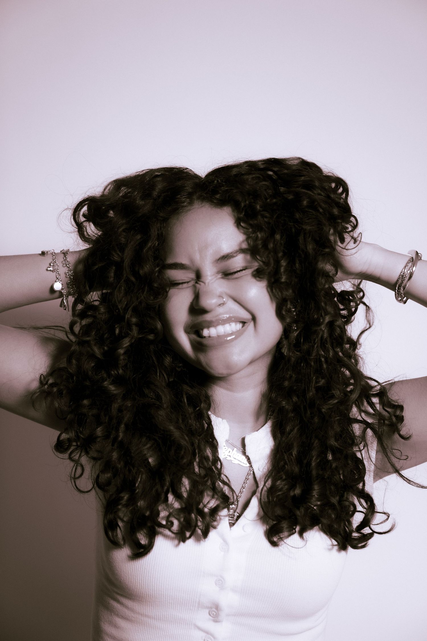 Portrait of someone with natural curly dark hair and a joyful expression against a pink background.