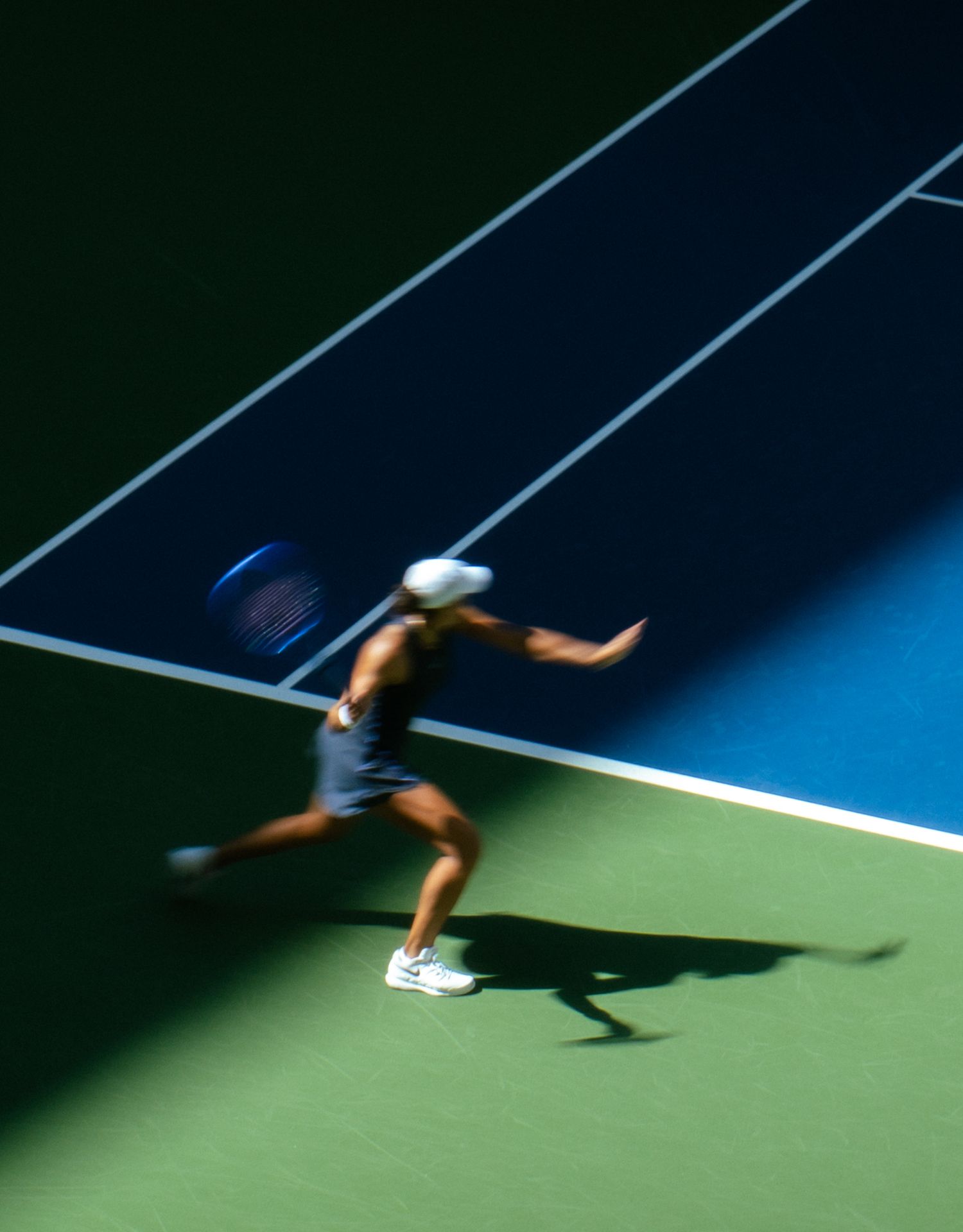 Motion blur captures a tennis player stretching horizontally to return a shot on a blue and green court.