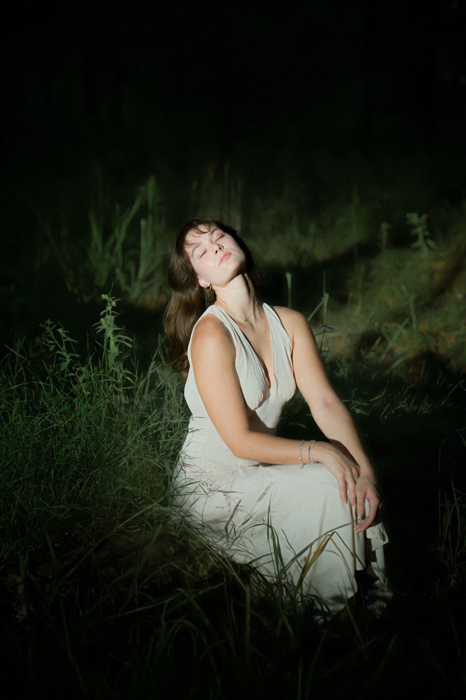 Moody evening portrait with person in white dress against dark forest background.