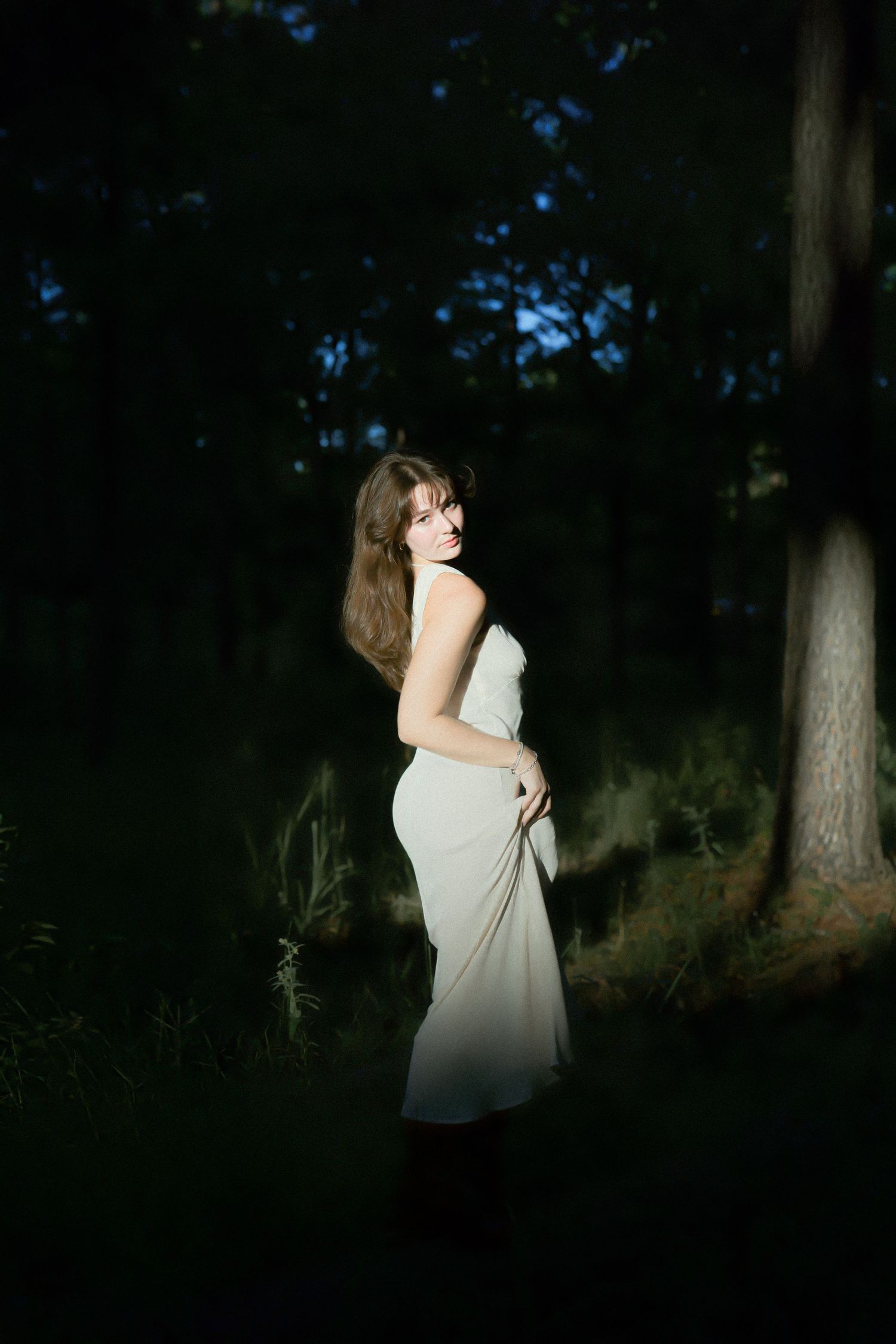 Artistic twilight portrait among pine trees with dramatic shadows and lighting.