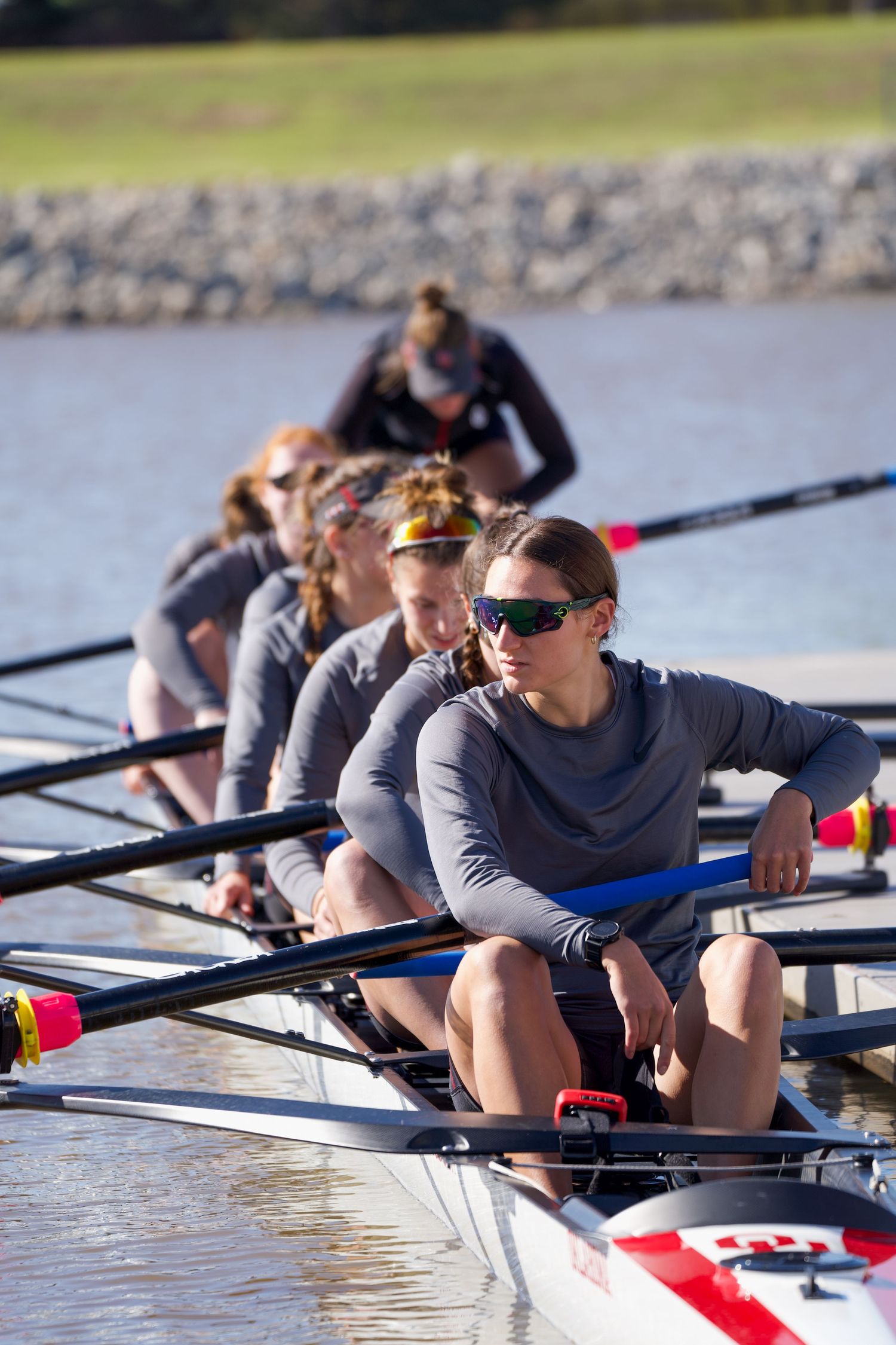 Closeup of rowing team members in grey shirts lined up in racing shell on water.