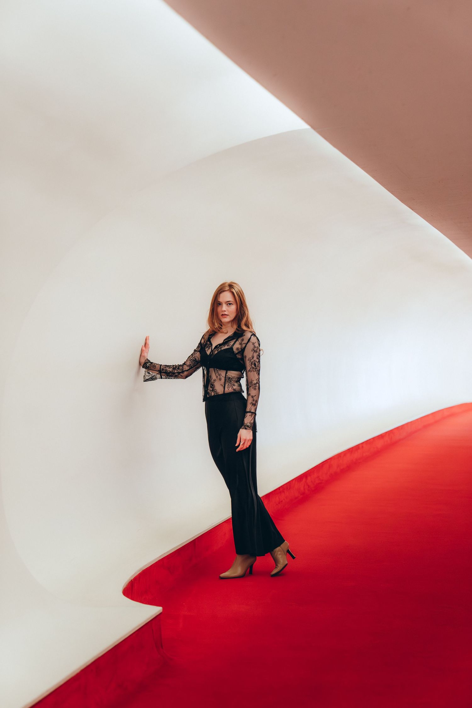 A woman in a black dress poses on a red carpet against a white wall in a dynamic photo series.