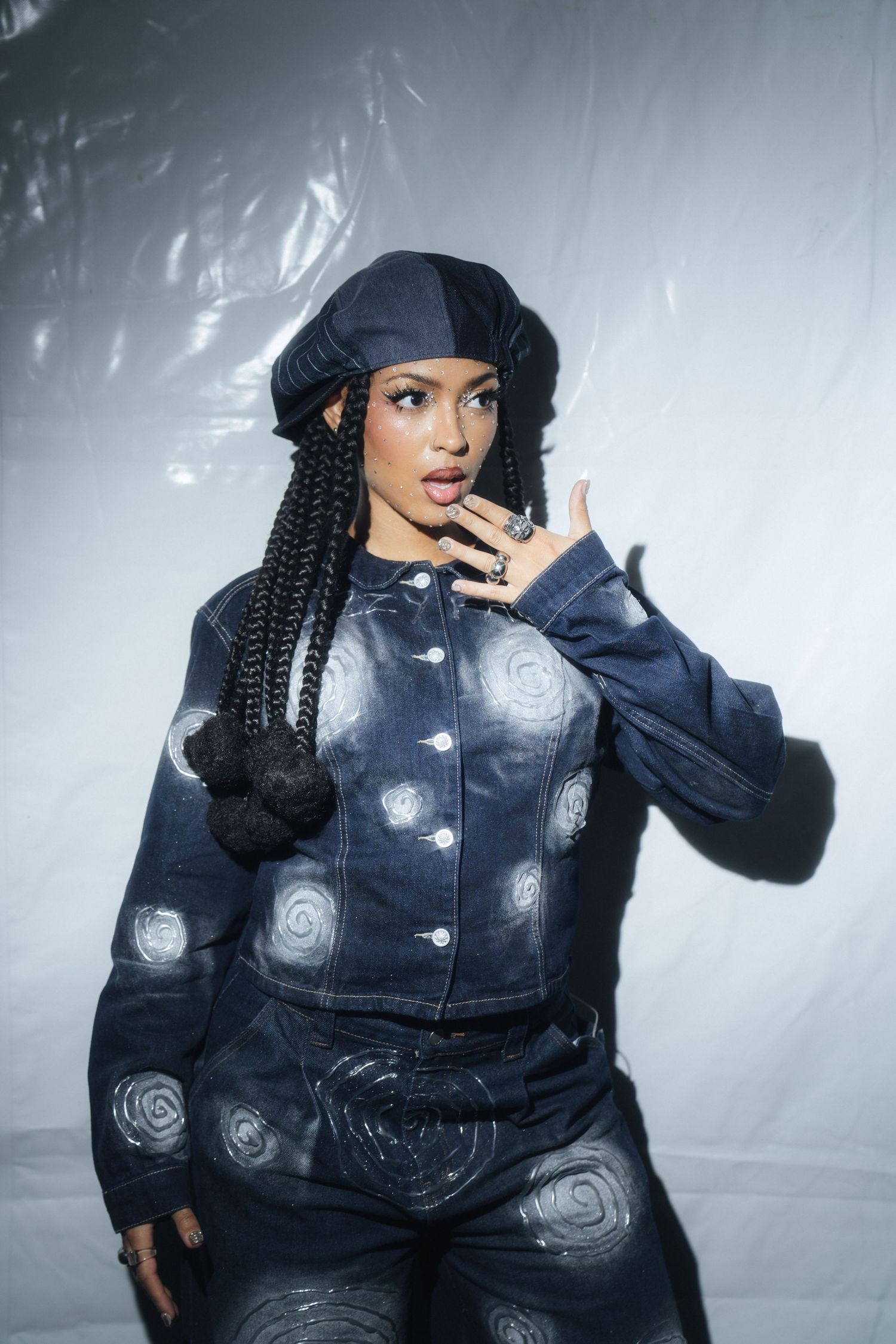 Model in navy blue puffer jacket with spiral designs poses against misty backdrop in fashion photoshoot series.