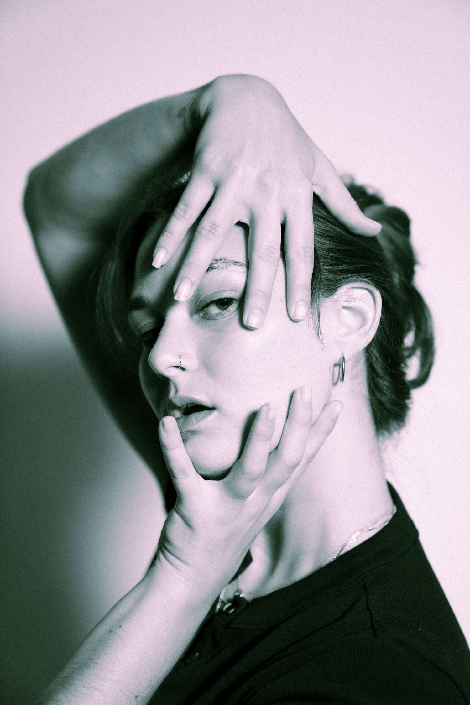 Artistic portrait with hands framing profile view wearing dark clothing in dual-toned lighting effect.