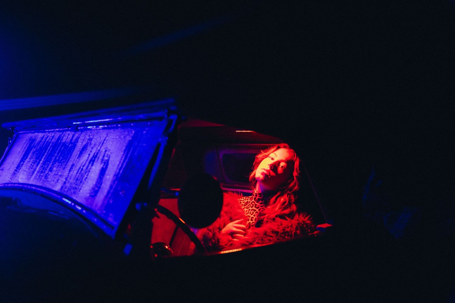 A DJ performs at night under dramatic blue and red lighting at an electronic music event.