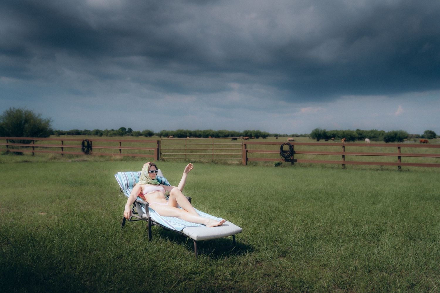 Someone lounges on a reclining chair in a grassy field with dark storm clouds looming overhead.