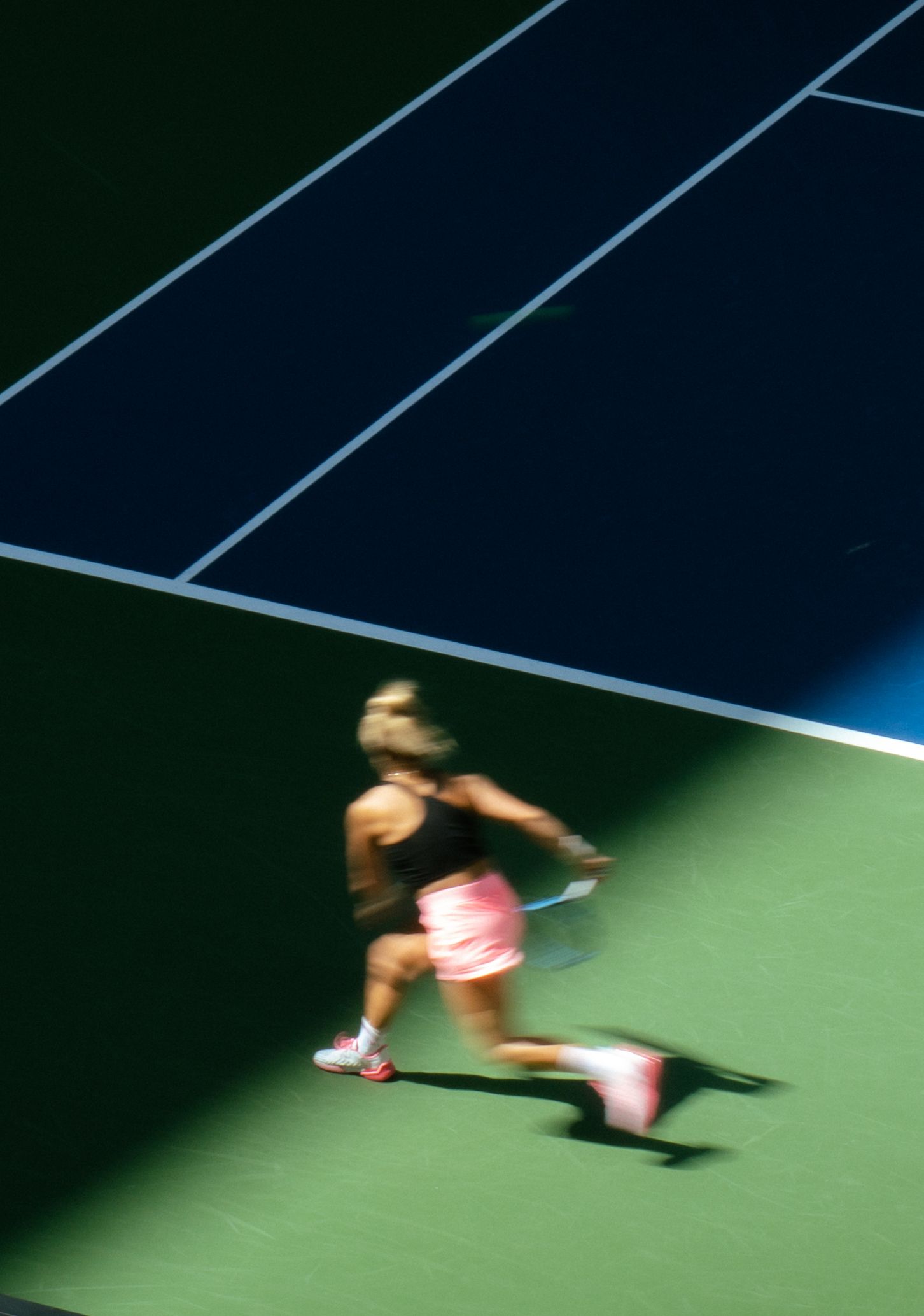 Tennis player in motion on court captured with motion blur effect during competitive match on hard surface.