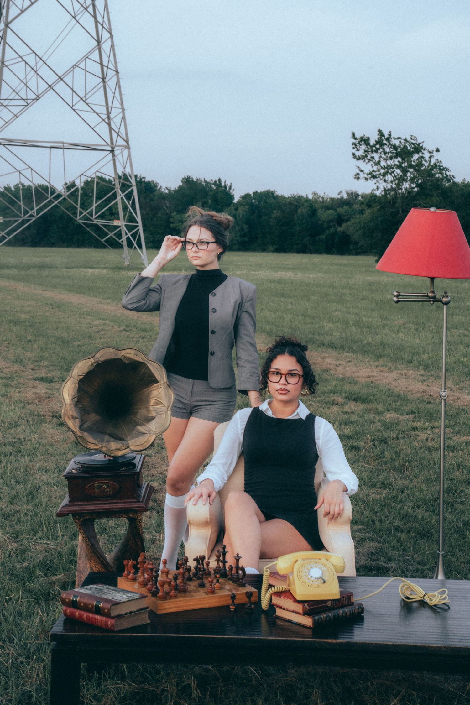 Two people playing chess at an outdoor table with a vintage gramophone and power lines in the background.