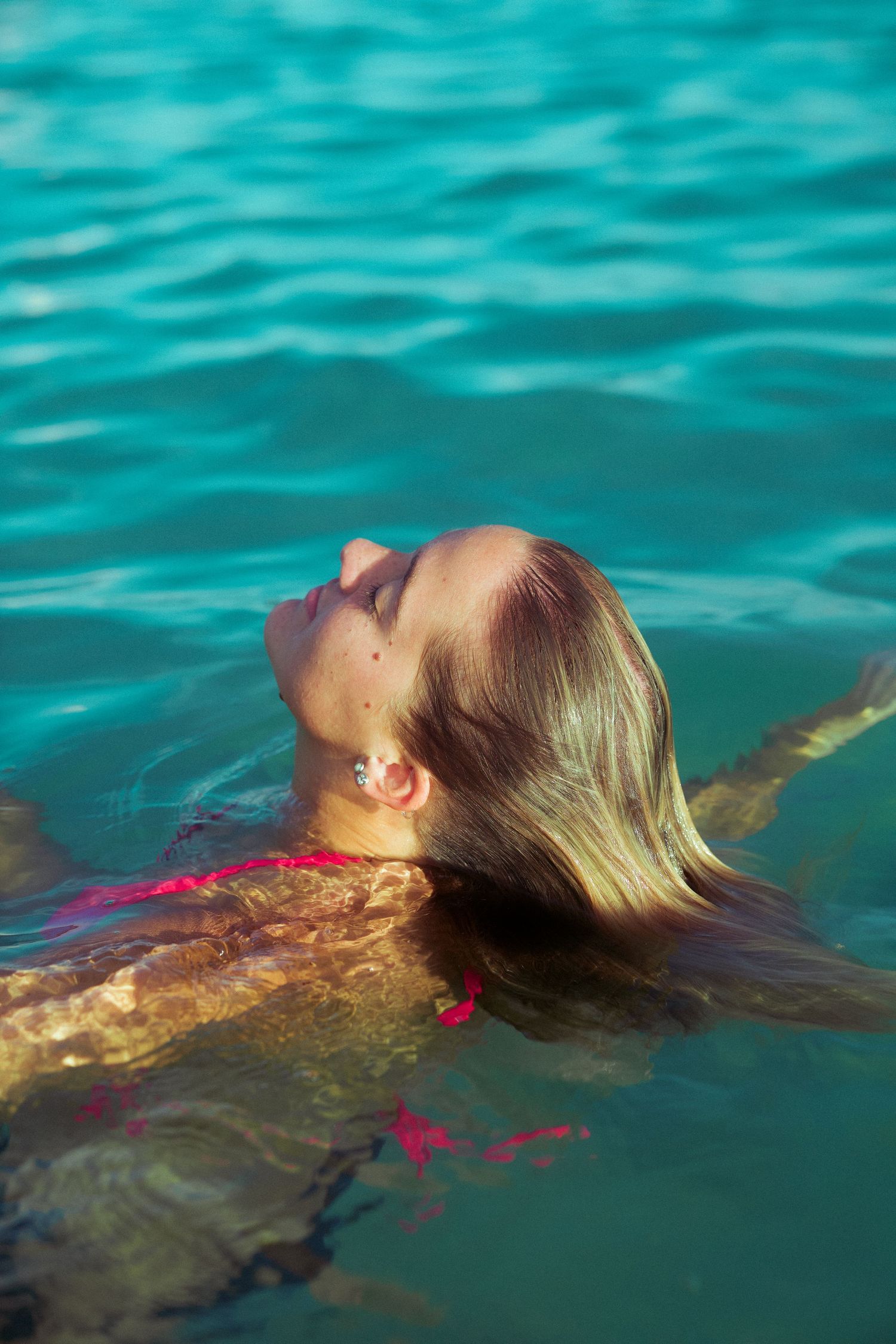 Person floating peacefully in clear turquoise water with blonde hair spread out.