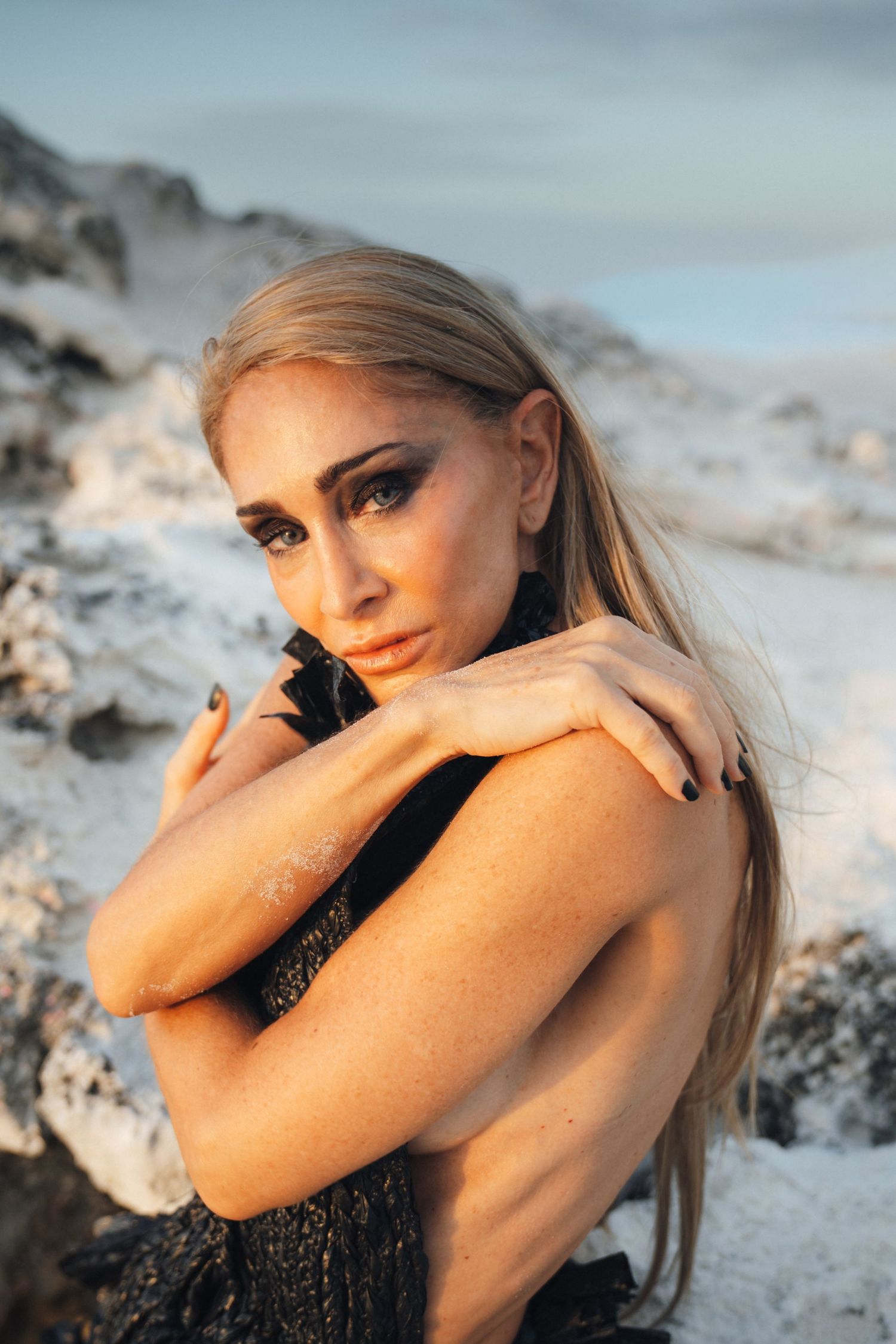 Artistic portrait series of a woman with blonde hair posing on sand during golden hour lighting.
