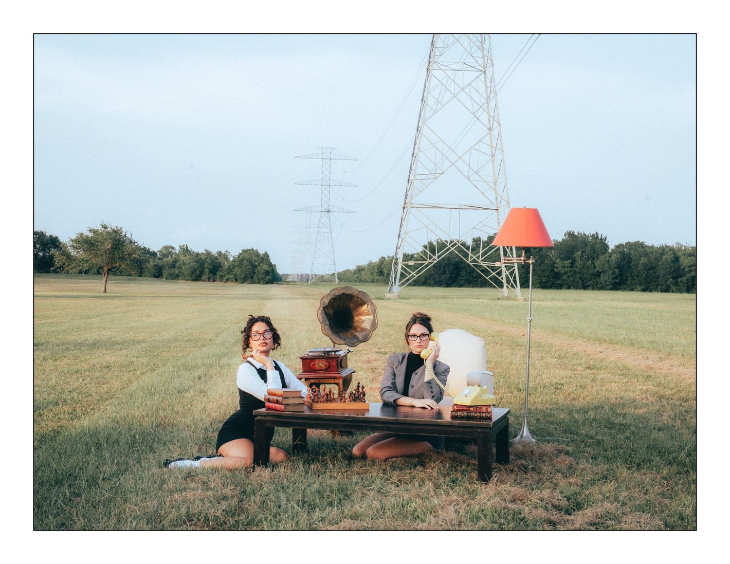 People enjoying a picnic at a wooden bench beneath an electrical transmission tower in a grassy field.