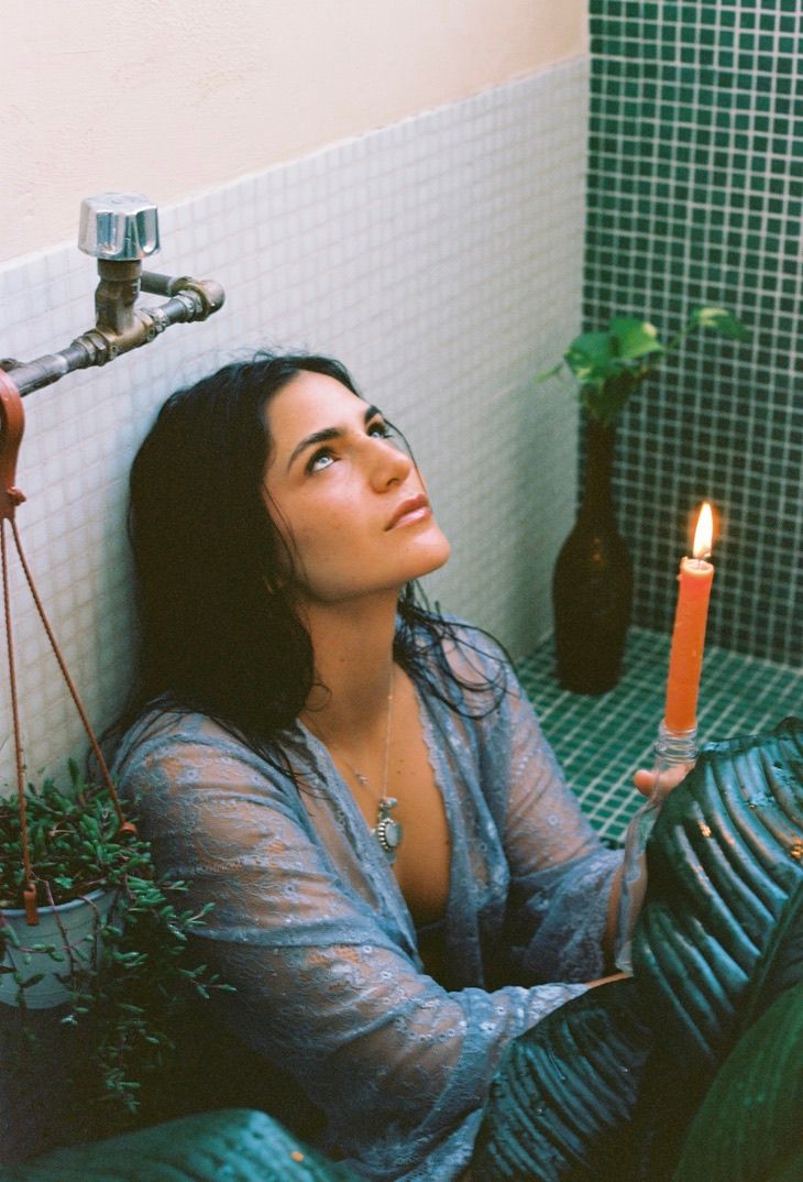 Dreamy candlelit bathroom portrait with green tile and plants creating peaceful ambiance.