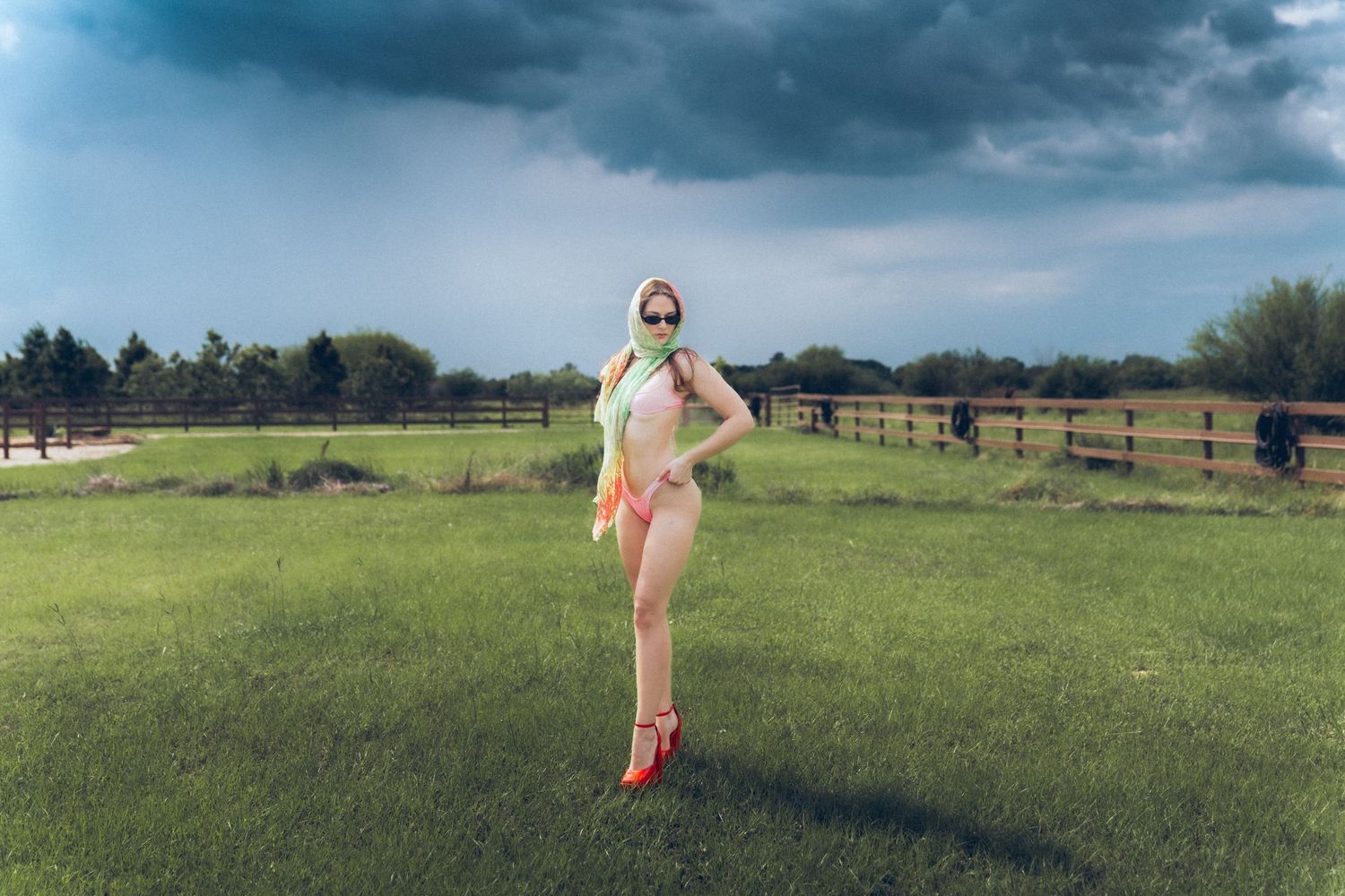 Person in vintage-style swimsuit strikes a playful pose in a grassy field with storm clouds gathering overhead.