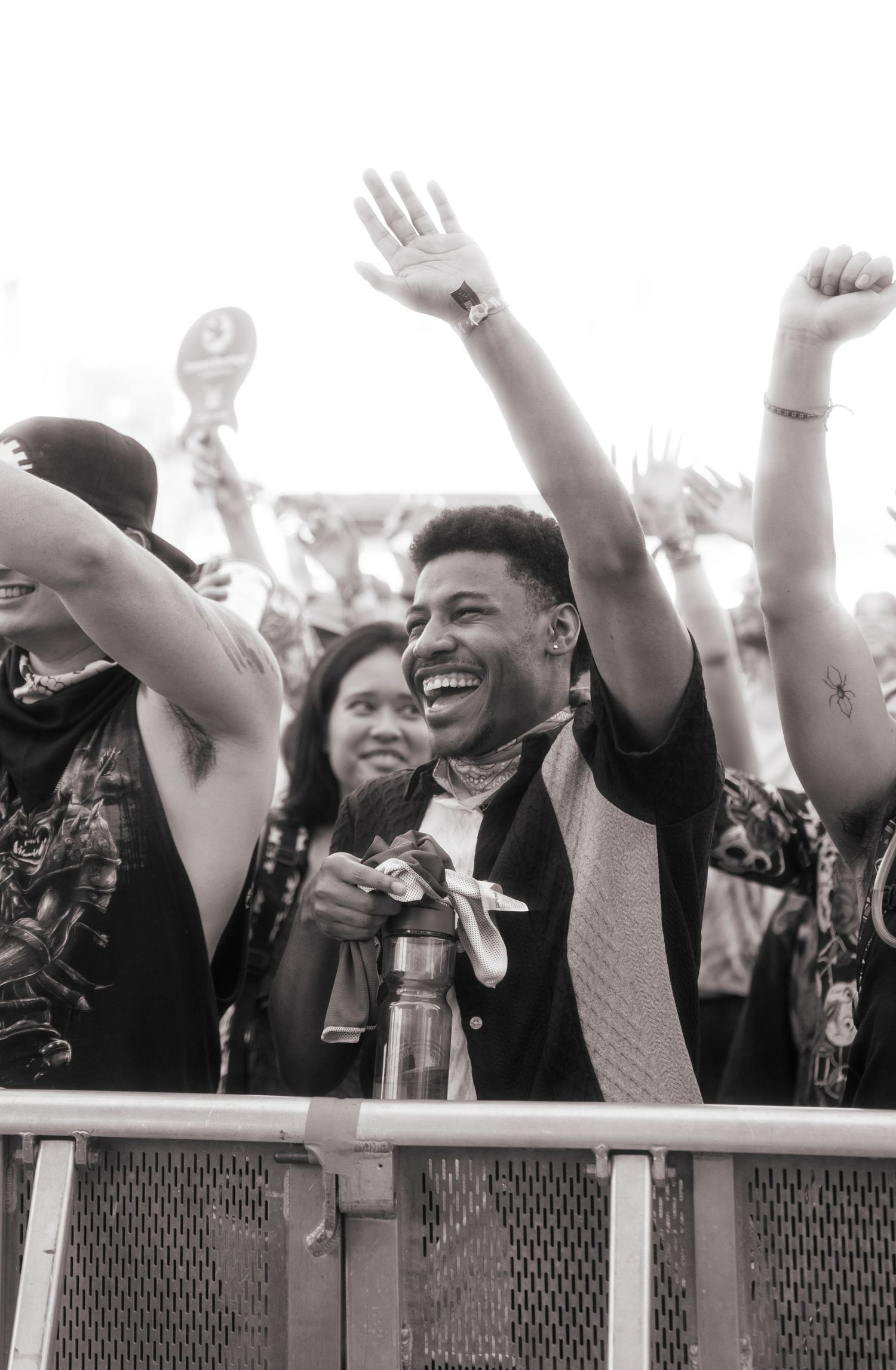 Enthusiastic concert crowd cheers and raises their hands at a music festival barrier in black and white.