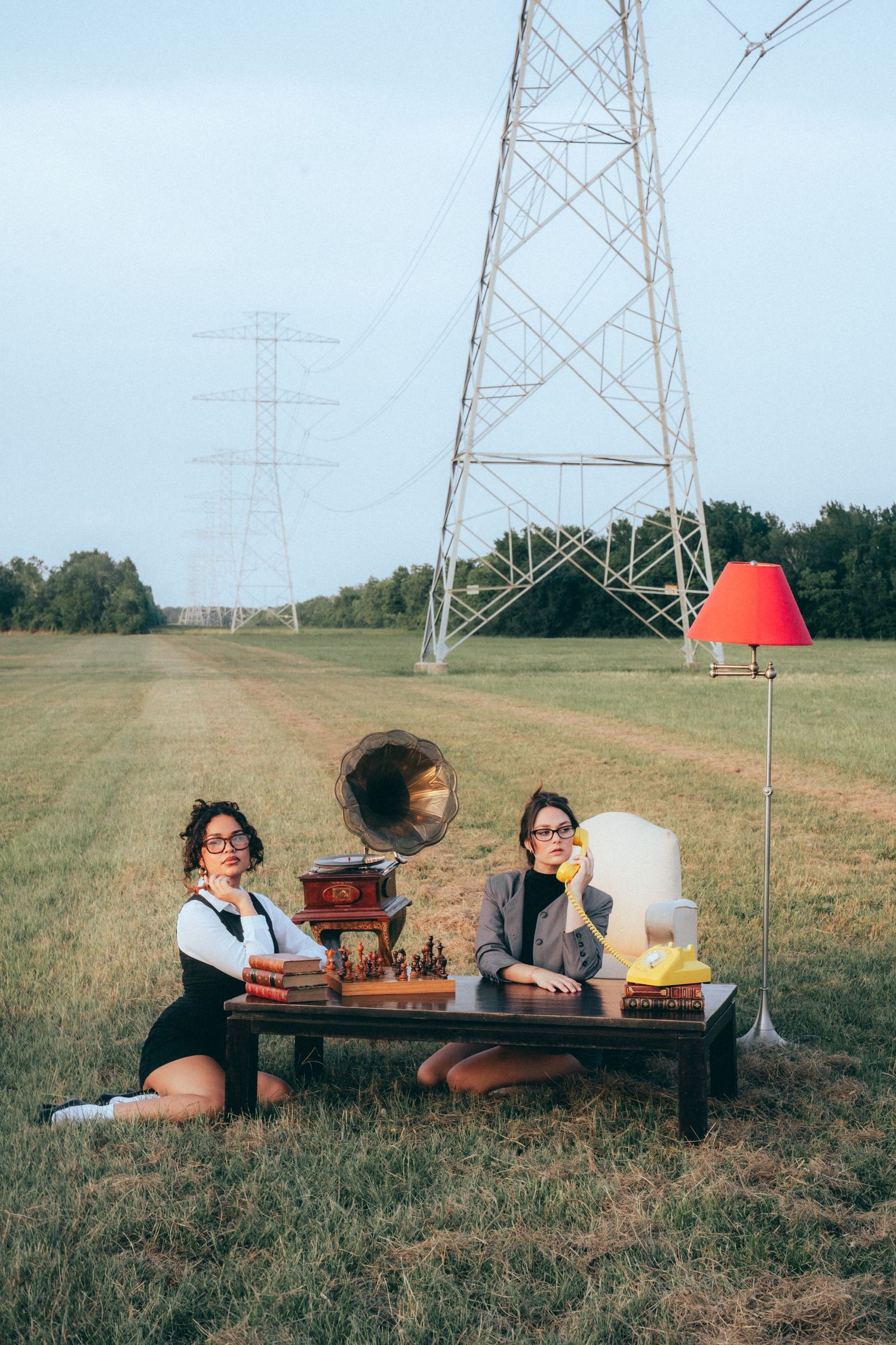 Two people having tea and snacks at a vintage-style setup beneath electrical transmission towers in an open field.