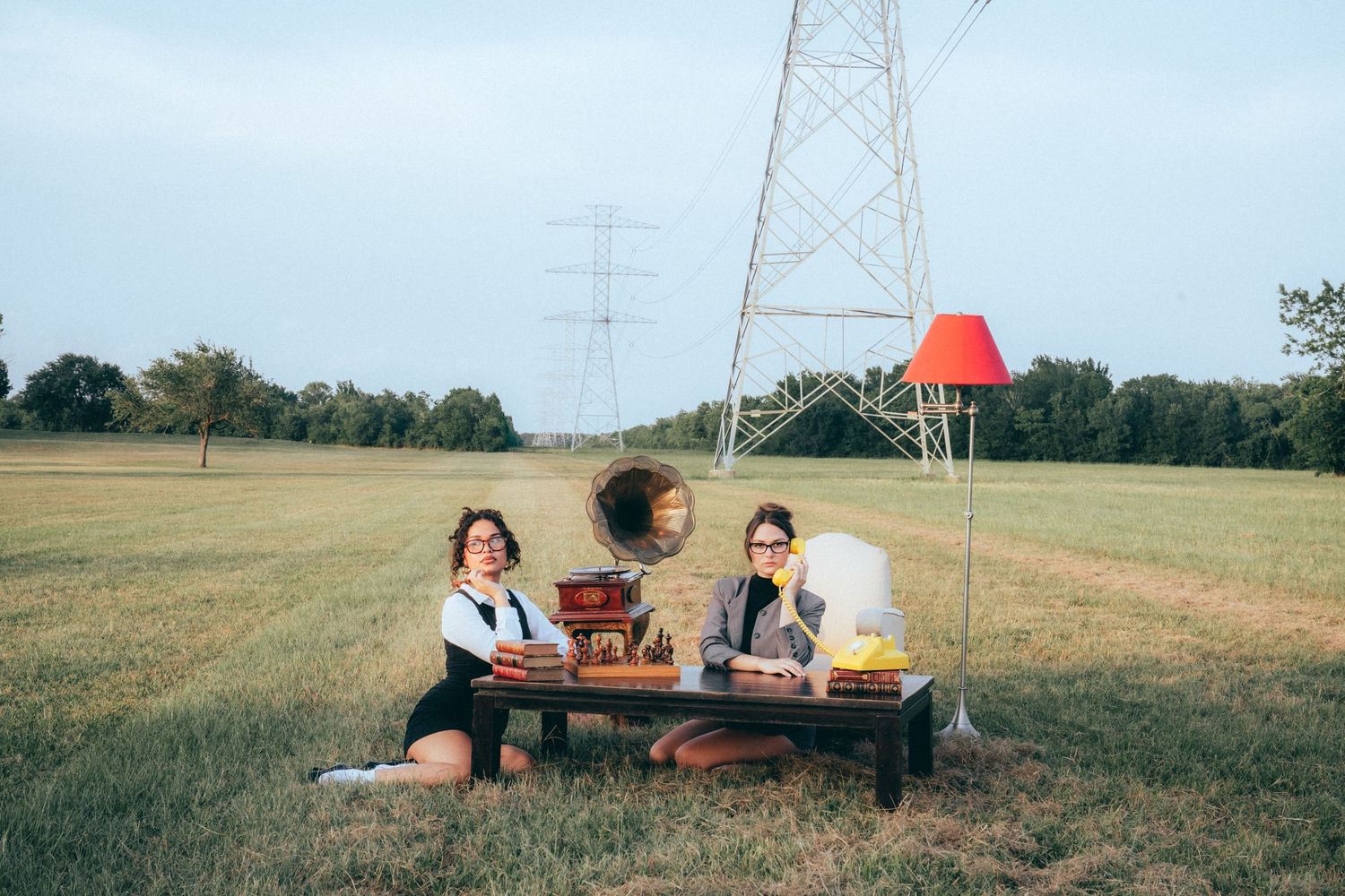 People lounging on a picnic blanket beneath power transmission towers in a grassy field at sunset.