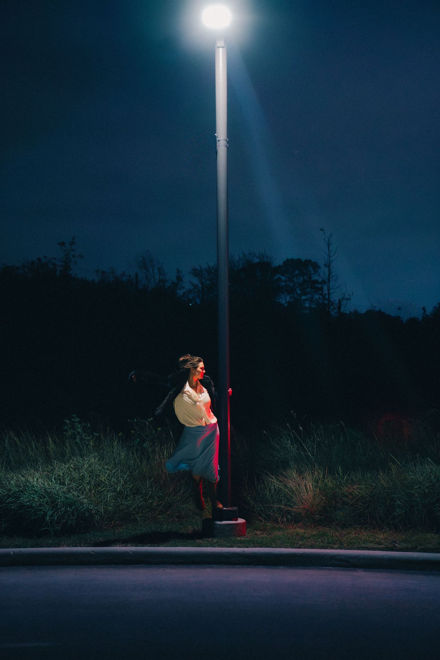 A lone figure stands under a bright street lamp at night creating a dramatic silhouette against the dark surroundings.