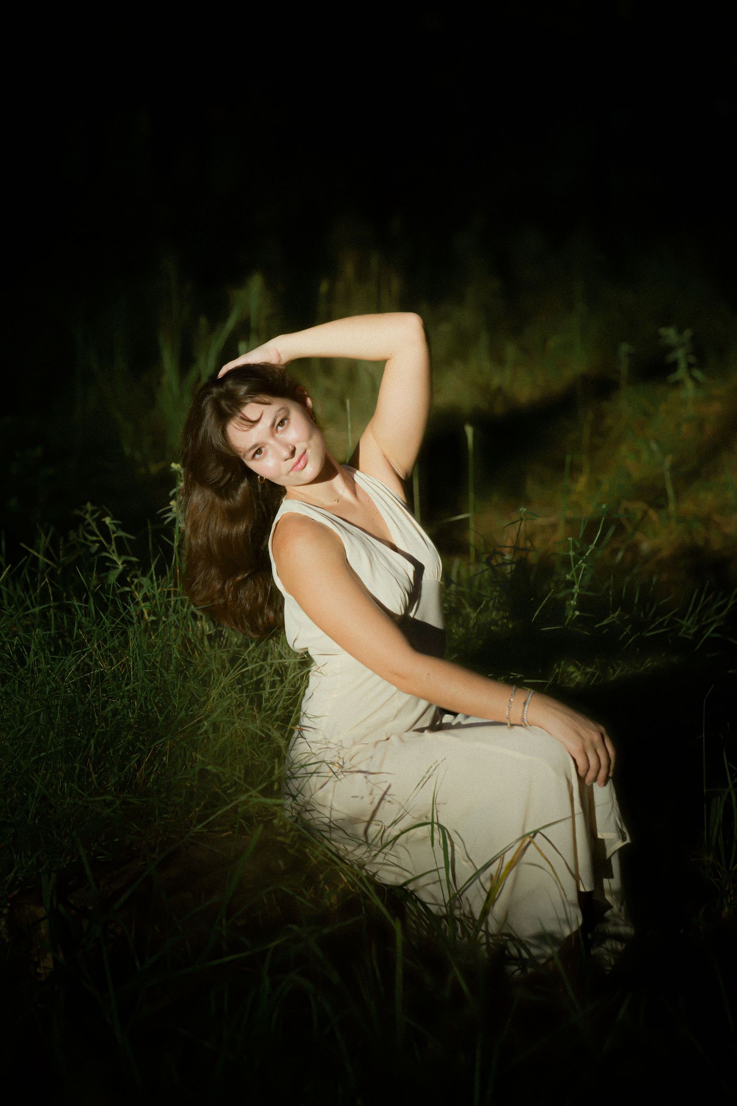 Atmospheric night portrait of person in white dress surrounded by tall grass.