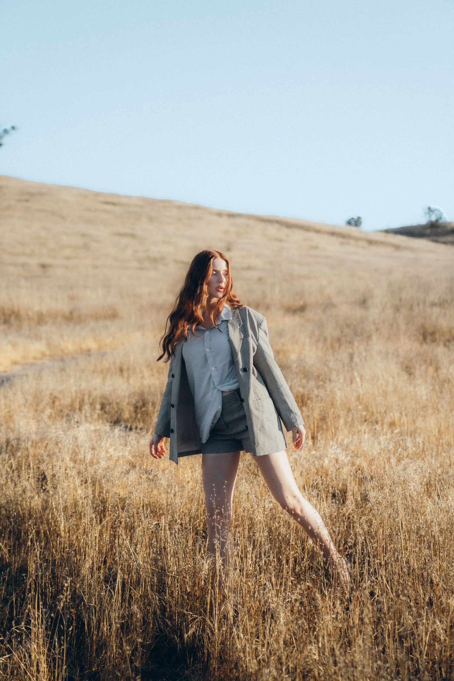 A person in casual attire dances joyfully through a golden field of tall grass during sunset.