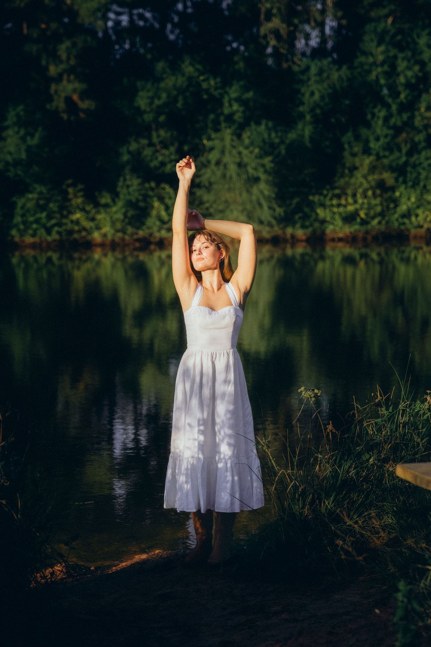 Ethereal scene of a white sundress-clad figure dancing by a reflective lake surrounded by trees.