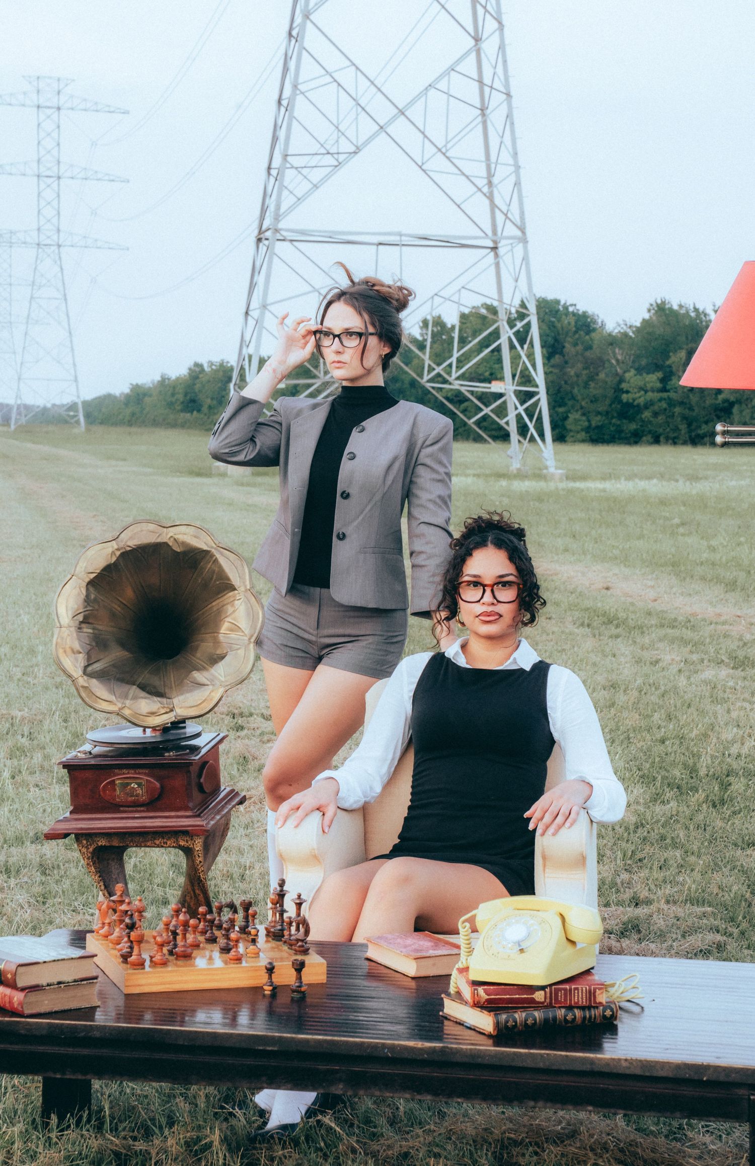 Vintage gramophone sits on wooden table with chess set and books under power lines in grassy field.