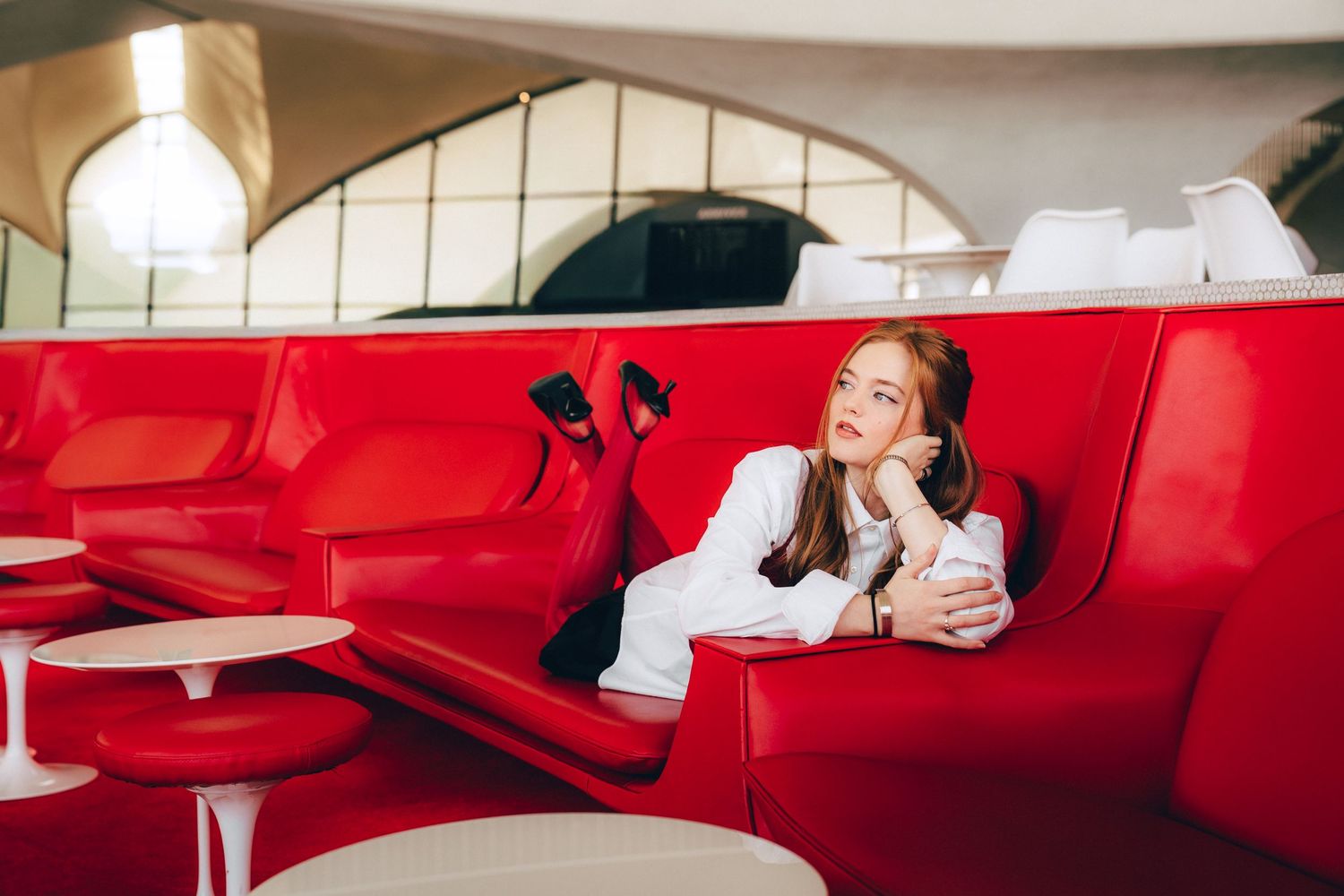 People relax on bright red leather booths in a modern restaurant interior with white tiled walls.