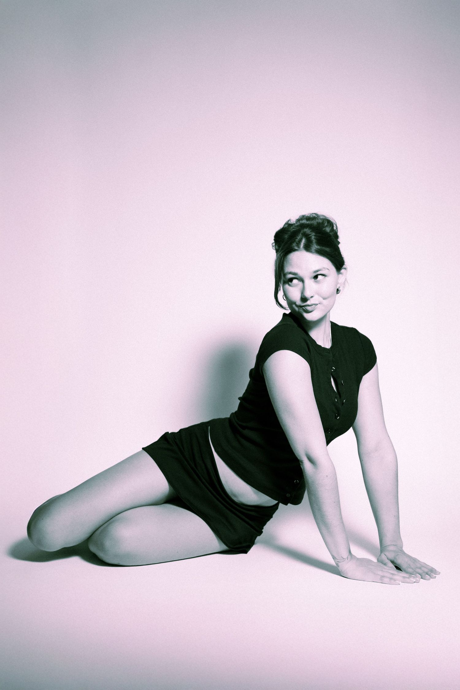 A vintage-style portrait photograph showing a person in a black dress posing against a pink background.