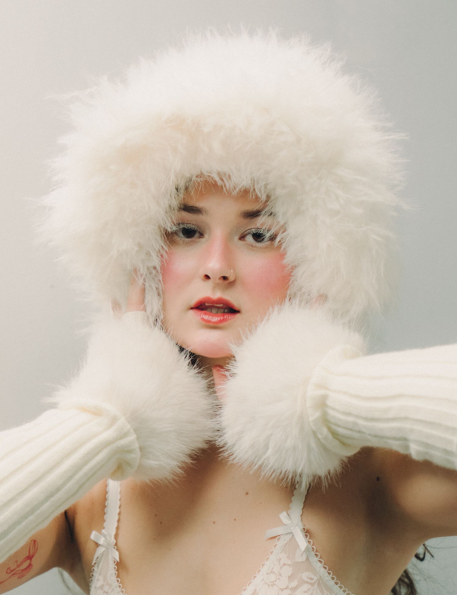 A fashion portrait featuring a fluffy white fur hat and matching gloves with a cream knit sweater against a light background.