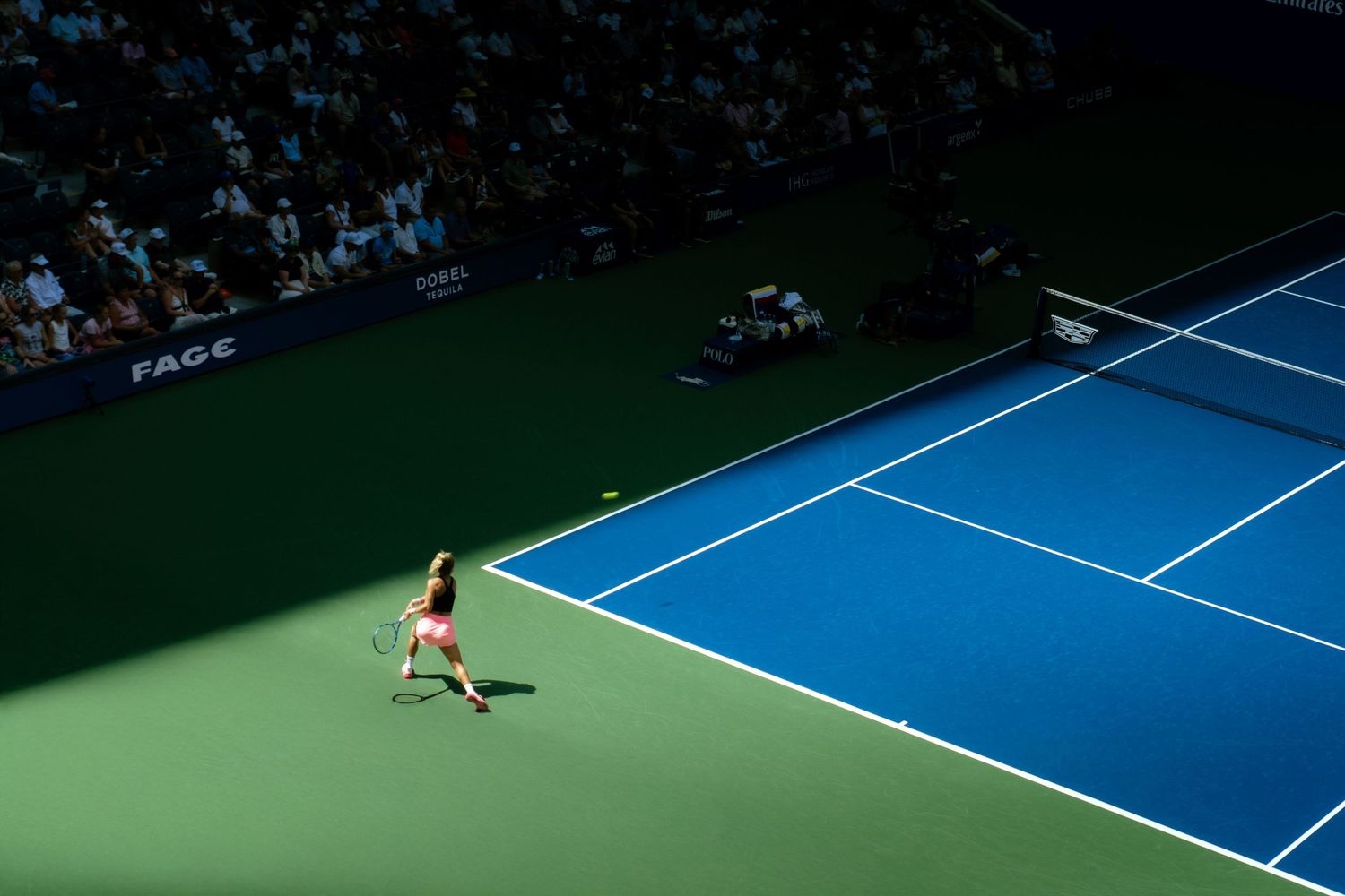 Tennis player on a vibrant blue and green court viewed from above during a professional match at a stadium.
