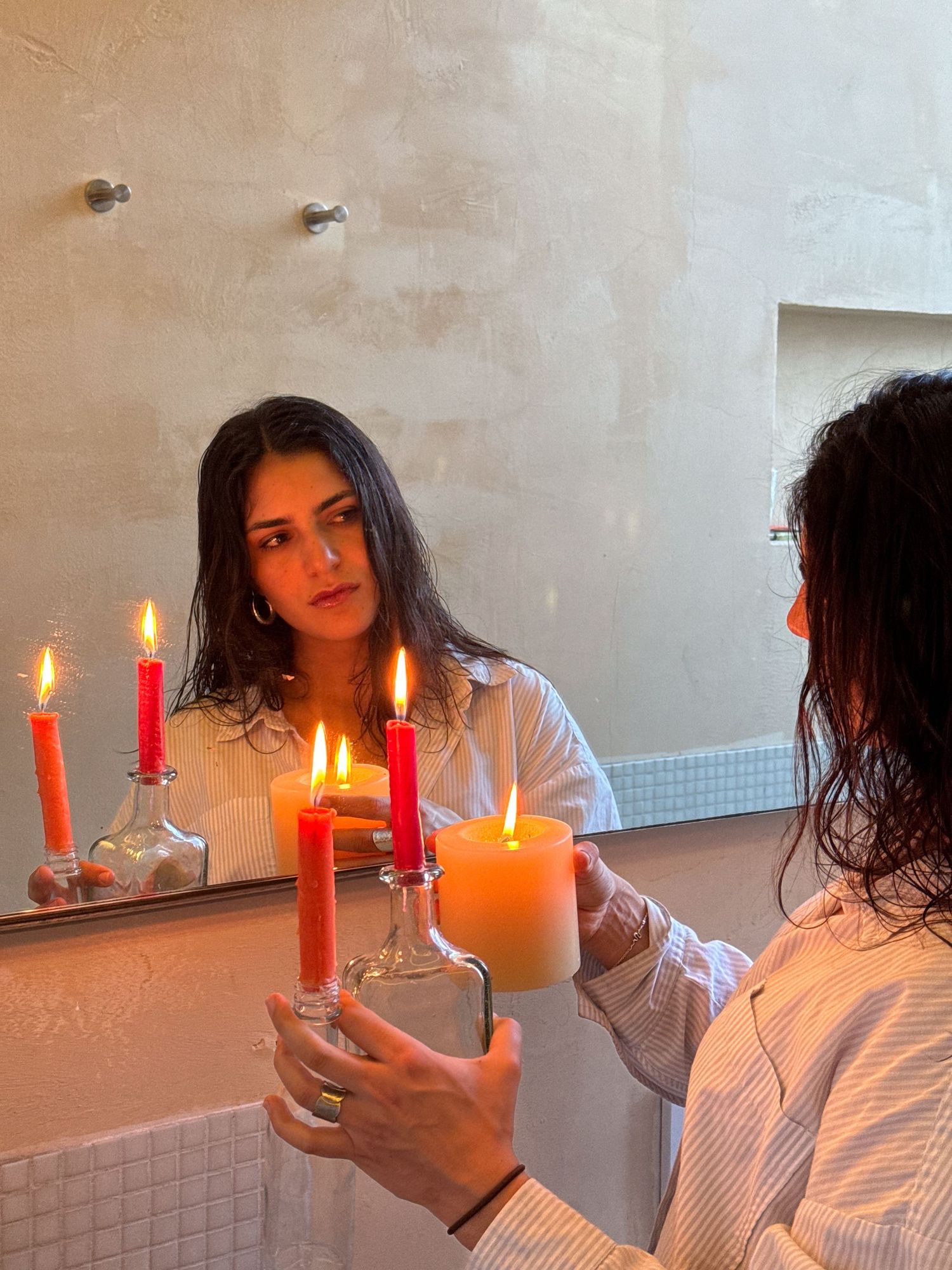 Moody bathroom scene with lit candles creating warm ambiance against tiled walls.